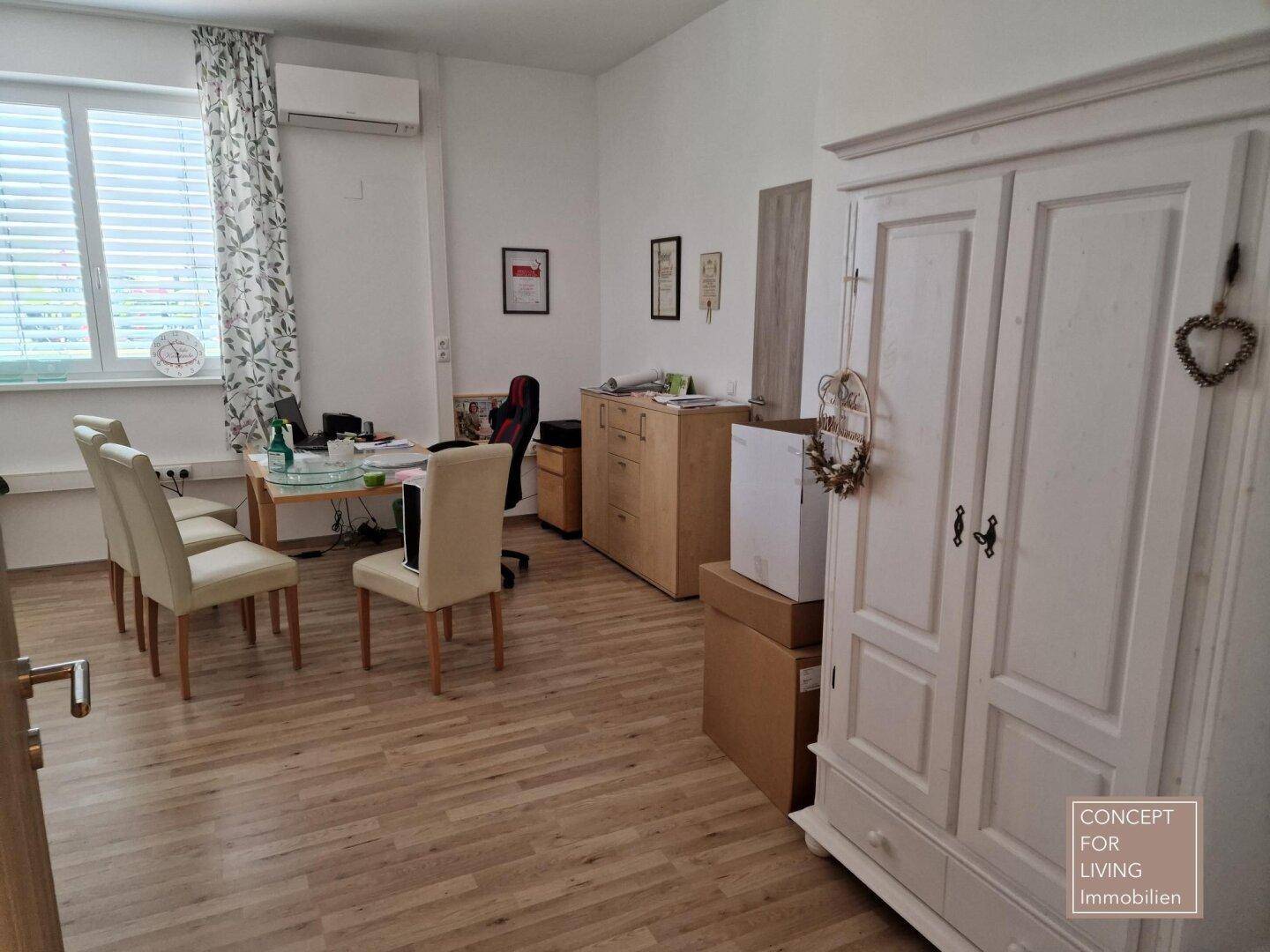Geräumiges Büro mit Holzboden, großem Schrank und einem Schreibtischbereich mit Stühlen.