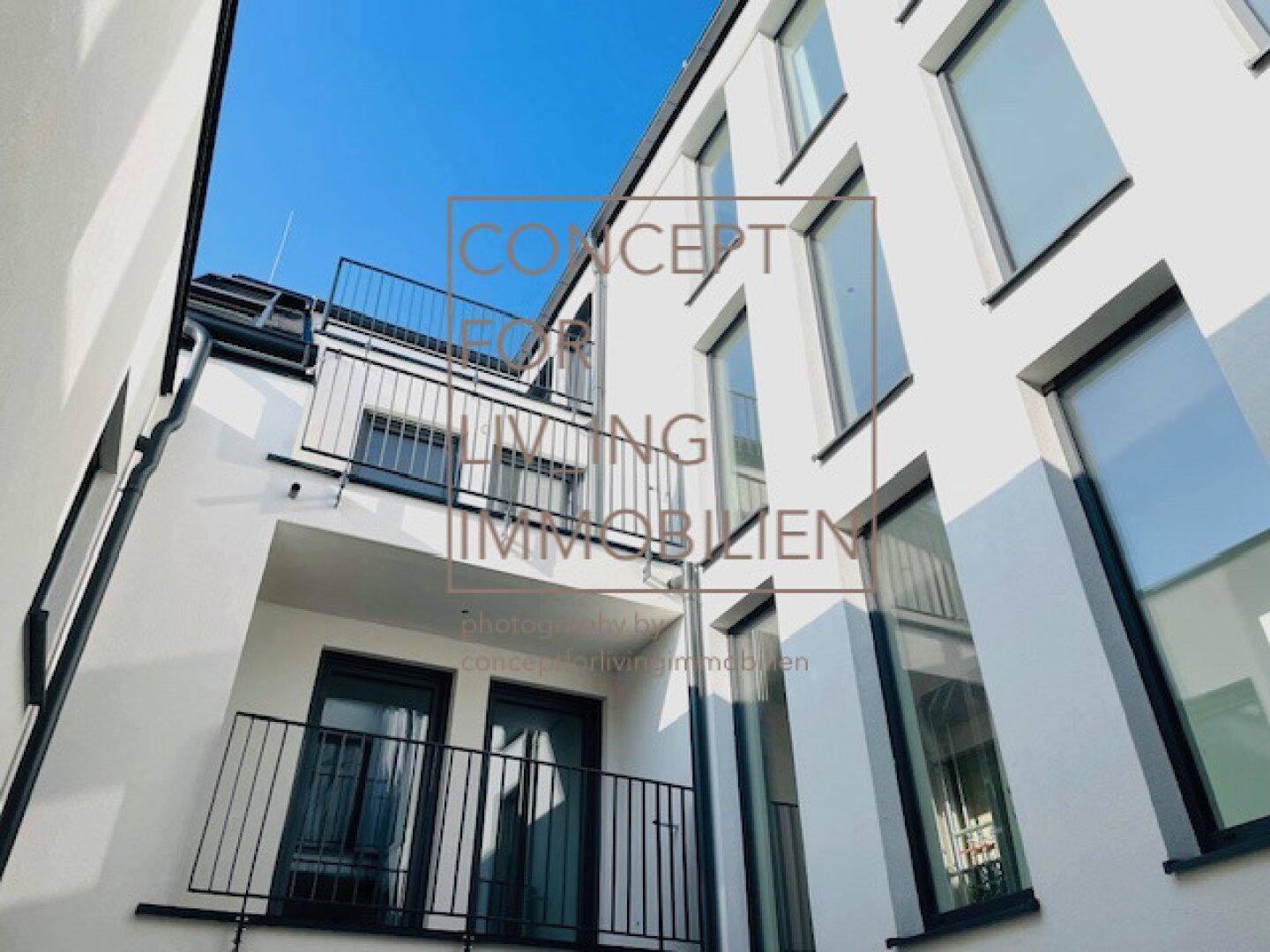 Moderne weiße Fassade eines Wohngebäudes mit mehreren Balkonen und Pflanzen.