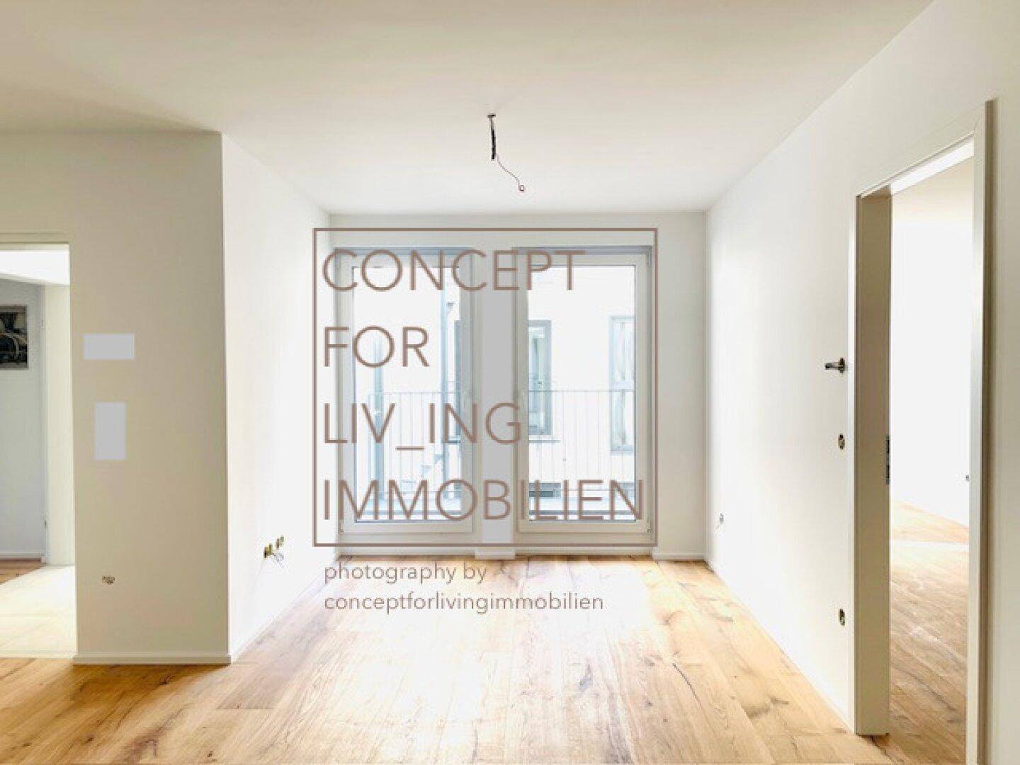 Heller, leerer Raum mit Holzboden und großem Fenster mit französischem Balkon.