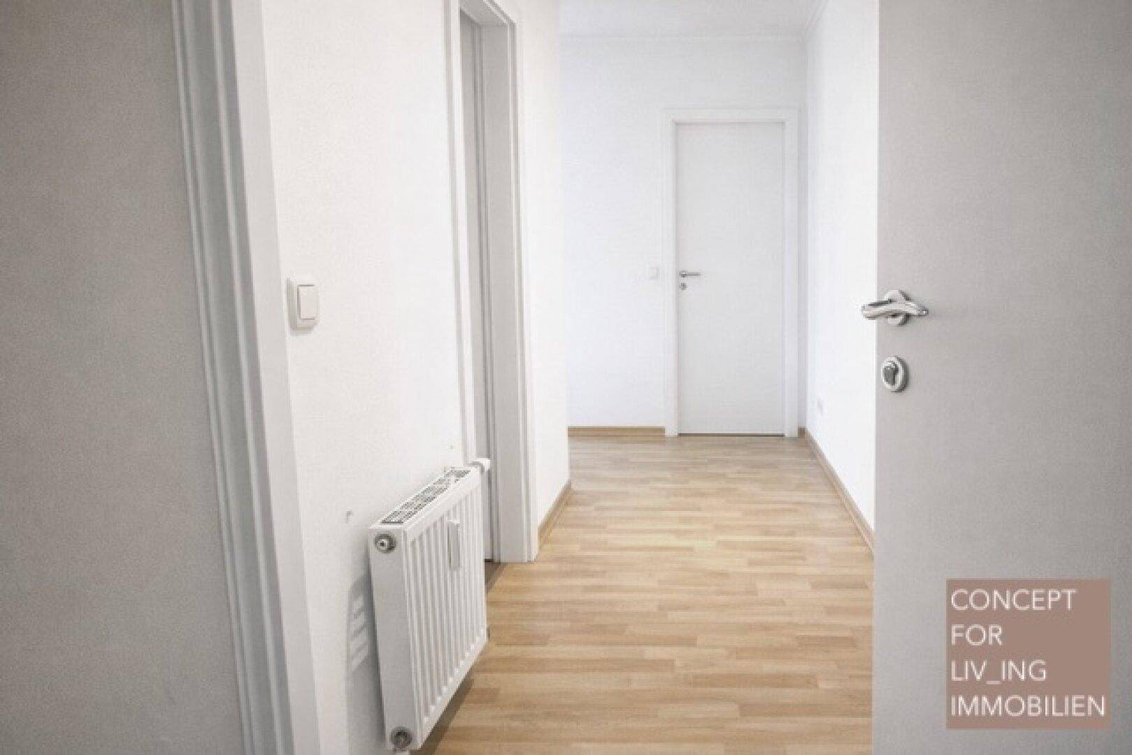 Heller Flur mit Parkettboden und weiß gestrichenen Wänden, führt zu weiteren Räumen.