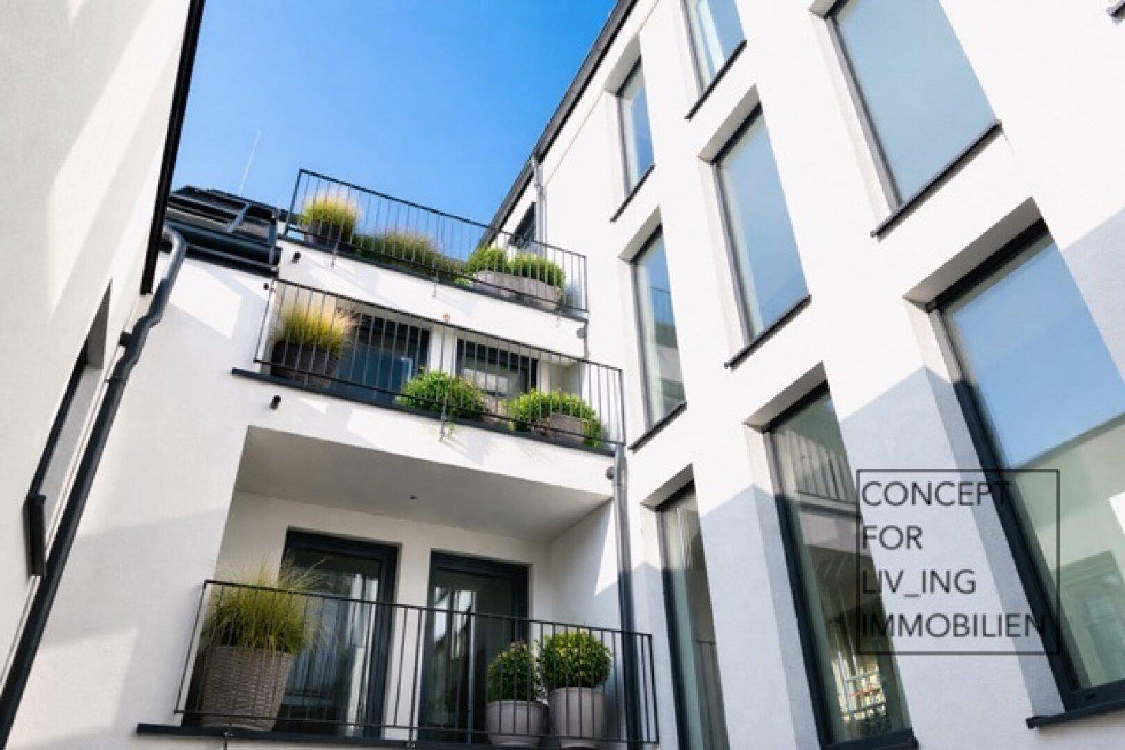 Moderne weiße Fassade eines Wohngebäudes mit mehreren Balkonen und Pflanzen.