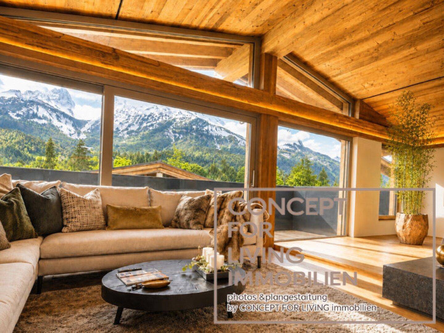 Gemütliches Wohnzimmer mit großem Sofa, Holzbalkendecke und beeindruckendem Bergblick durch Panoramafenster.