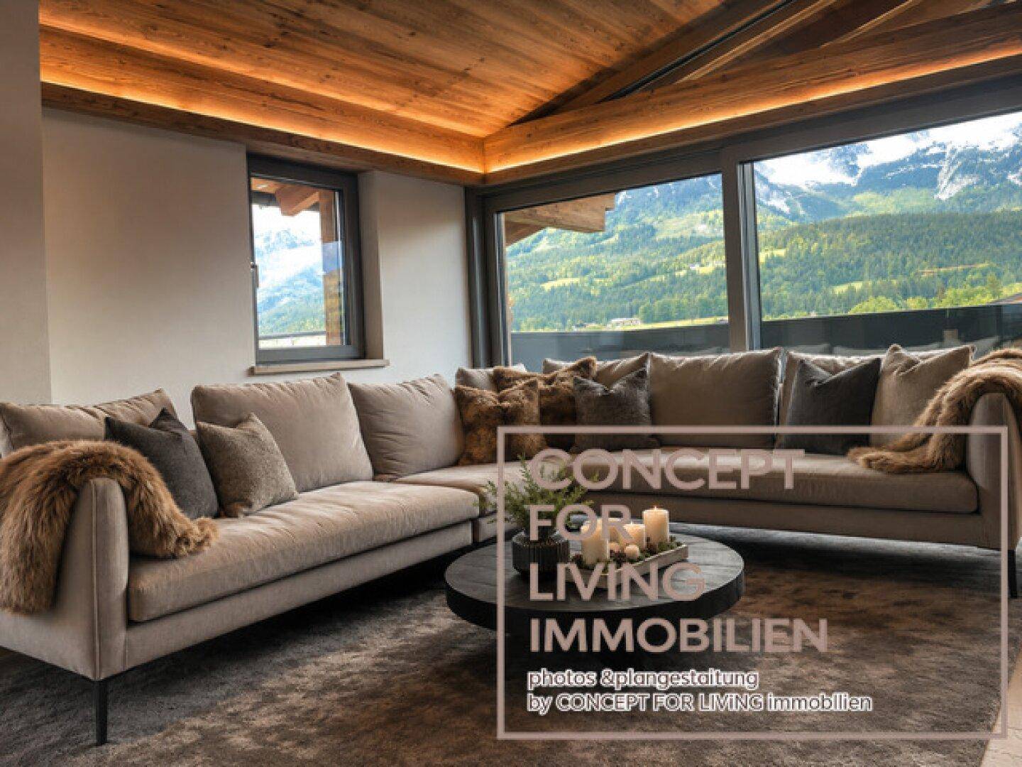 Helles Wohnzimmer mit beigem Ecksofa, Holzbalkendecke und weitem Blick auf die Berglandschaft.