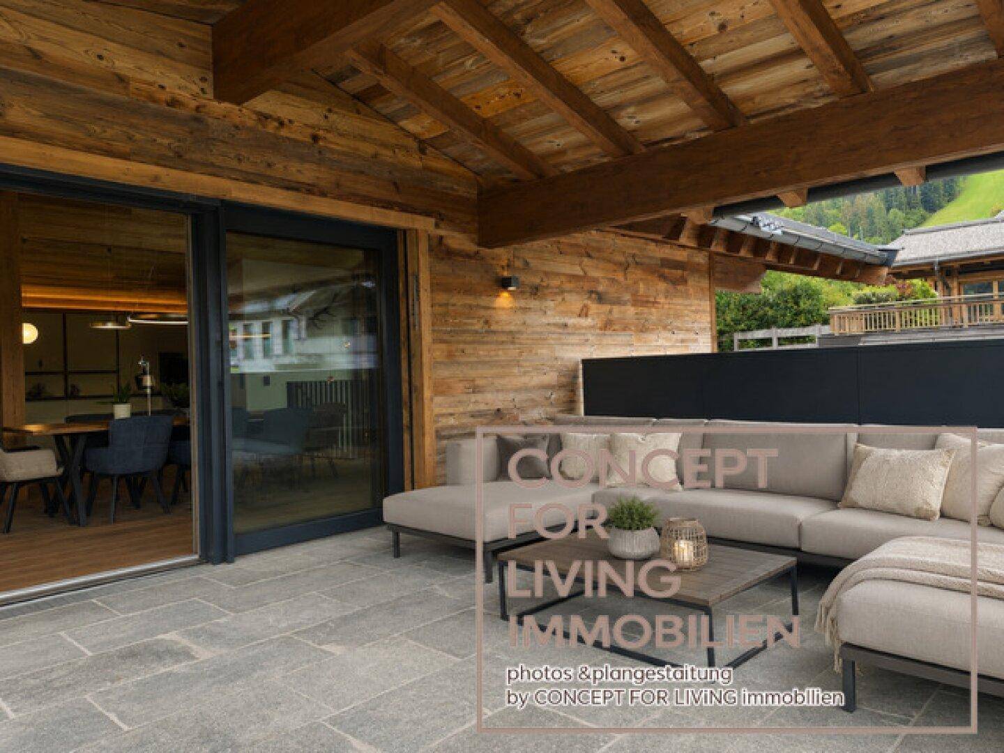 Stilvolle Terrasse mit Loungemöbeln und Zugang zum Essbereich, umgeben von alpiner Holzarchitektur.