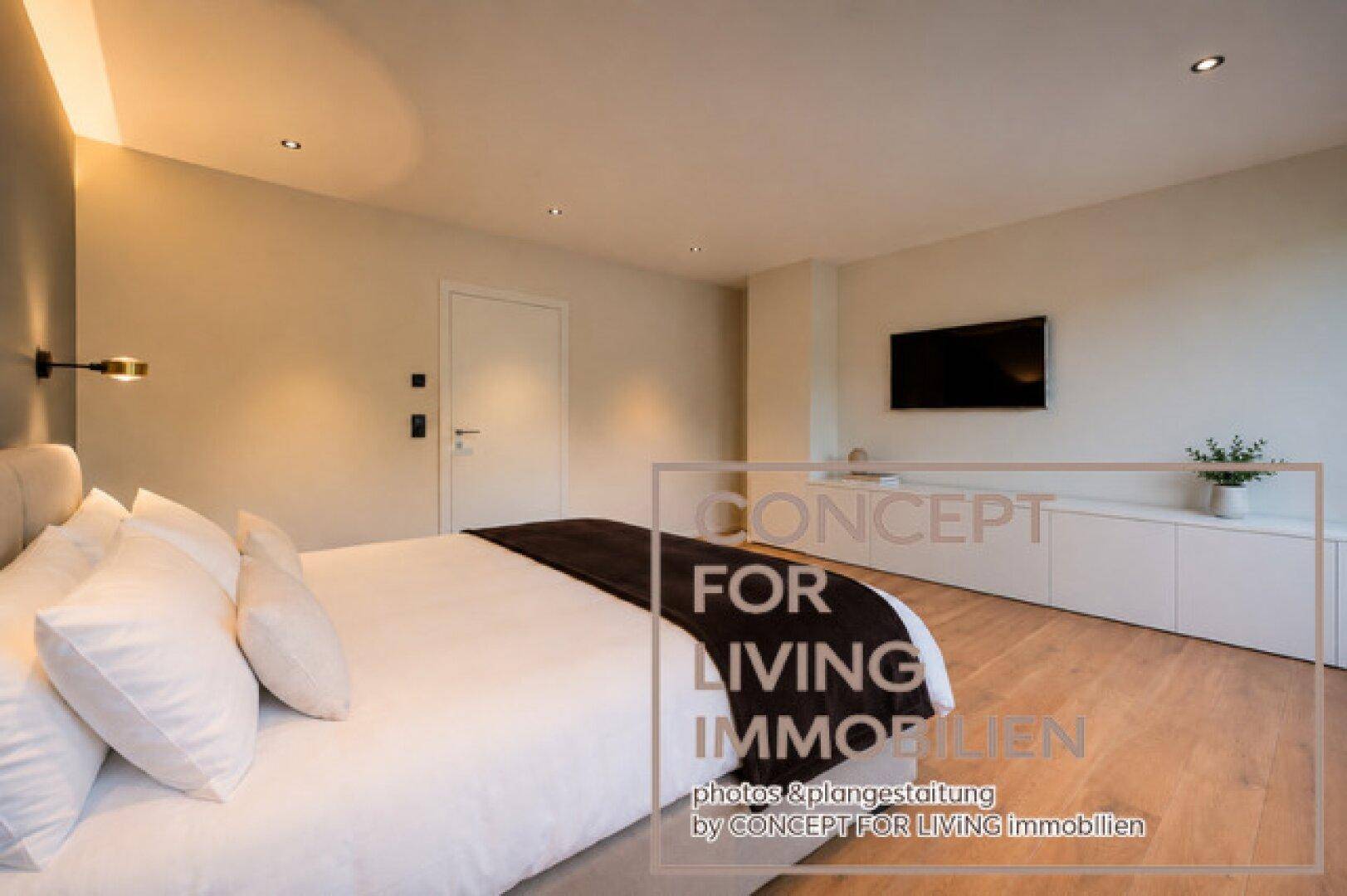 Modernes Schlafzimmer mit großem Bett, integriertem TV und schlichten, eleganten Möbeln.