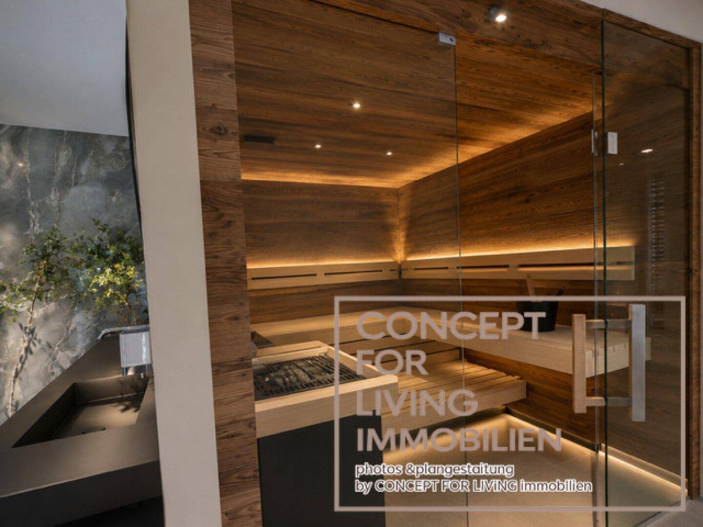Moderne Sauna mit Glasfront und indirekter Beleuchtung, integriert in einen luxuriösen Wellnessbereich.