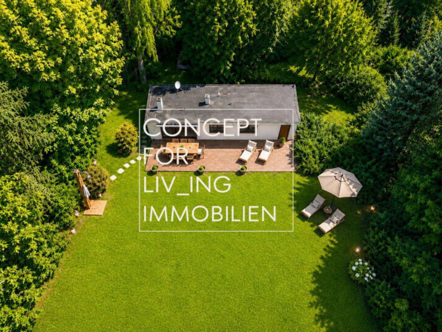 Luftaufnahme eines modernen Hauses mit großer Holzterrasse, umgeben von einem weitläufigen grünen Garten.