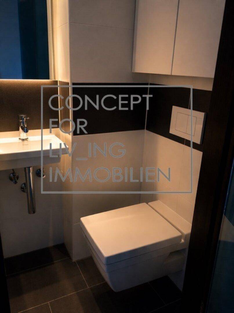 Modernes Gäste-WC mit wandhängender Toilette, kleinem Waschbecken und dunklem Fliesenboden.