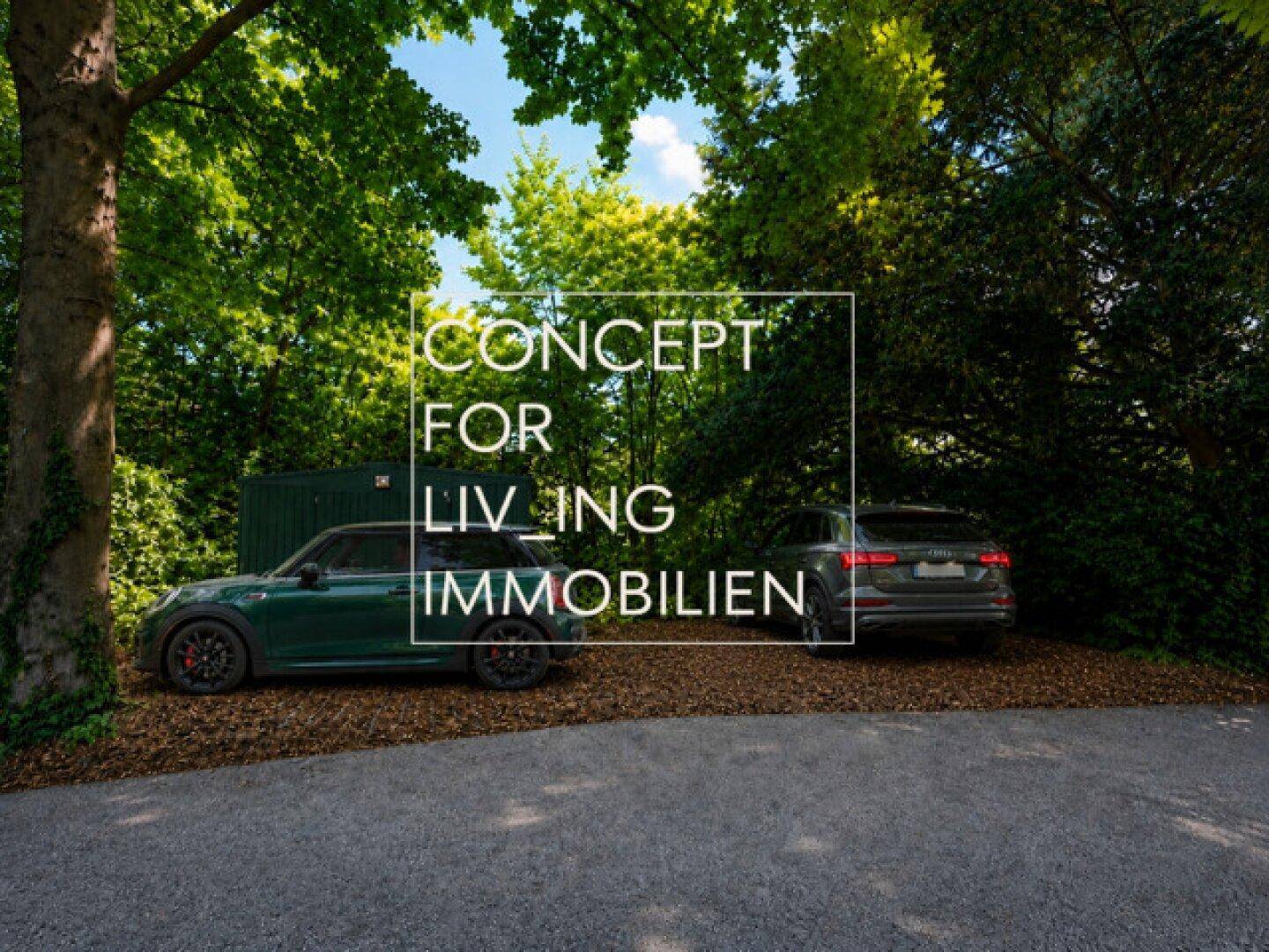 Parkplatzbereich umgeben von üppigem Grün mit zwei geparkten Autos unter Bäumen.