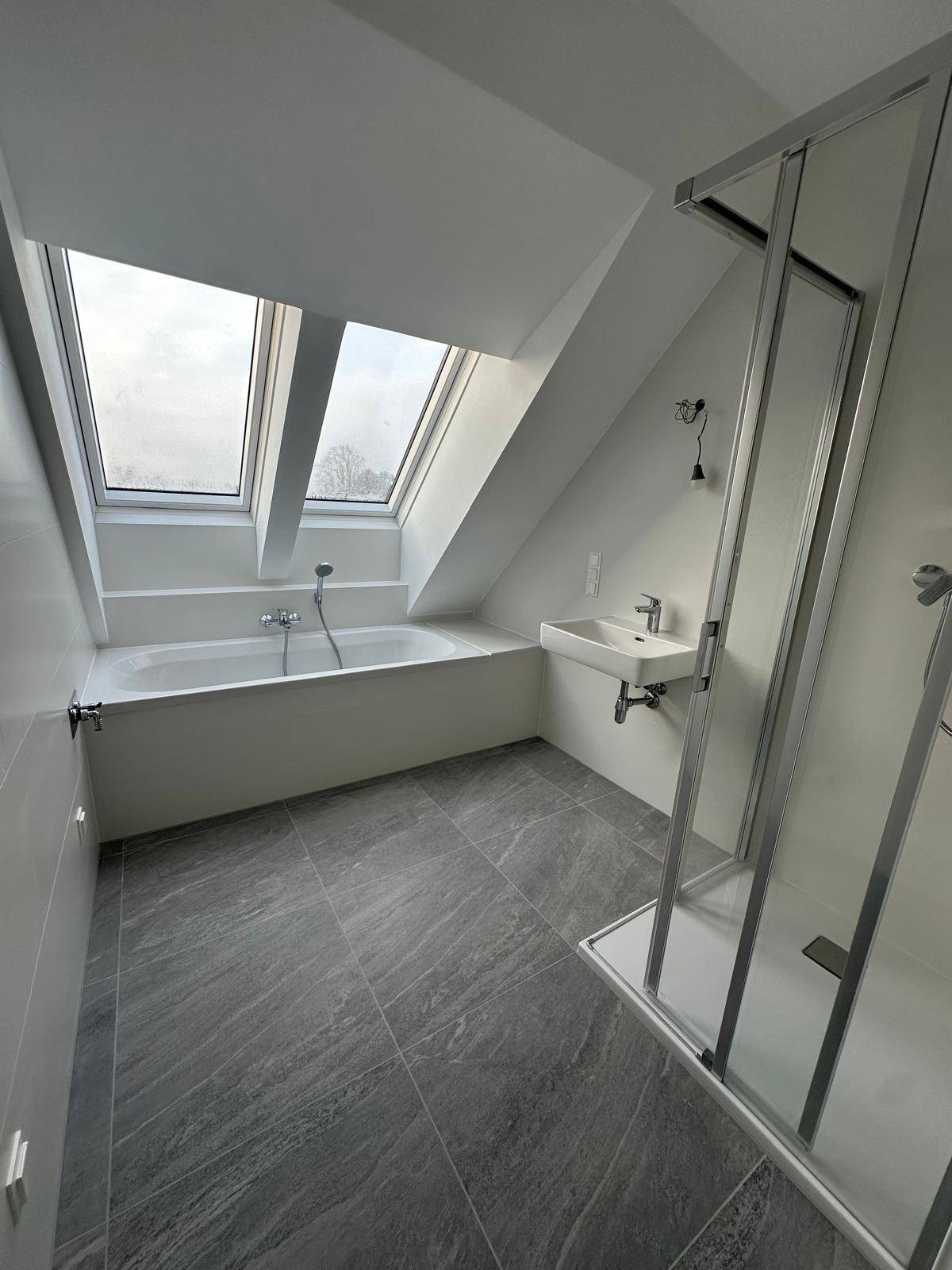 Helles Badezimmer im Dachgeschoss mit Badewanne, Dusche und Dachfenstern.