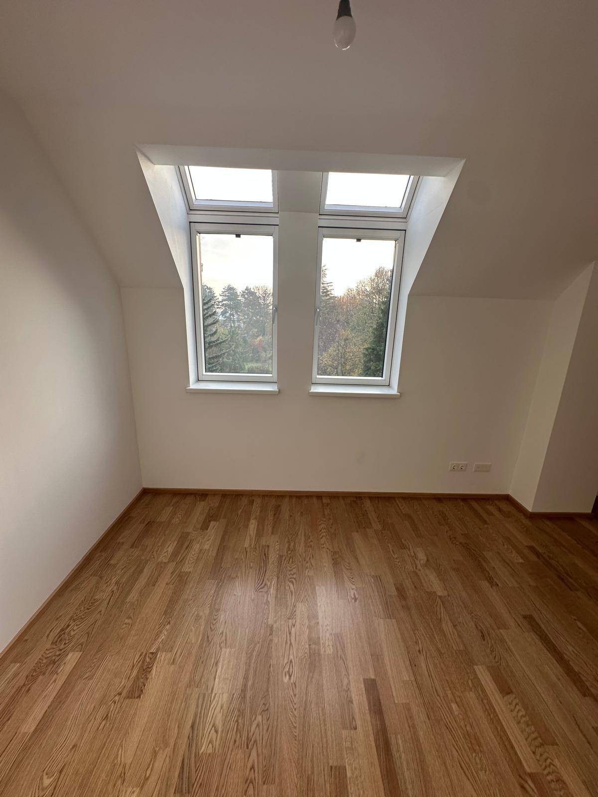 Helles Zimmer mit Parkettboden und zwei großen Dachfenstern, bietet viel Tageslicht.