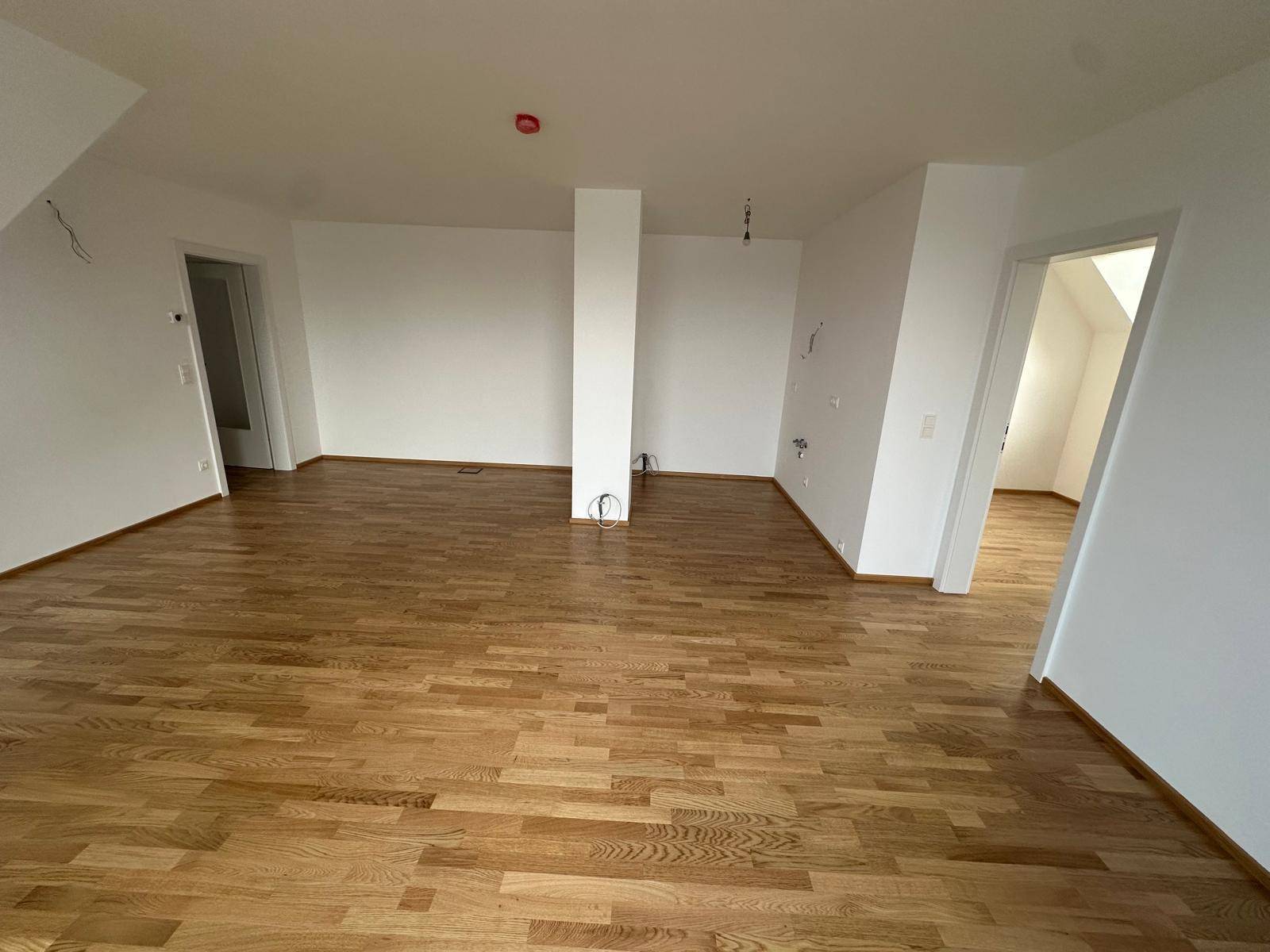 Geräumiger, heller Wohnbereich mit Holzboden und mehreren Zugängen zu anderen Räumen.