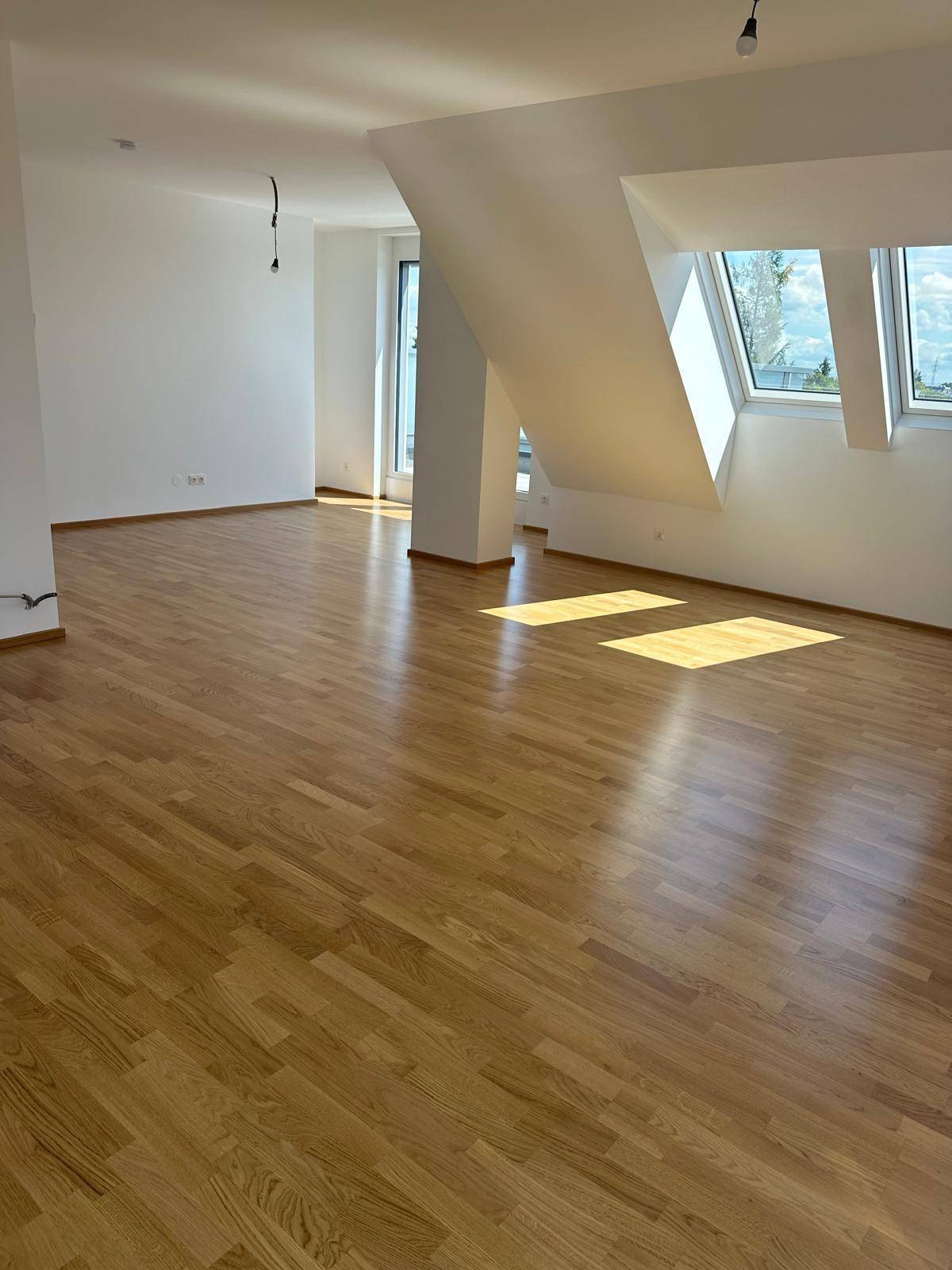 Lichtdurchfluteter Wohnbereich mit Parkettboden und großen Dachfenstern.