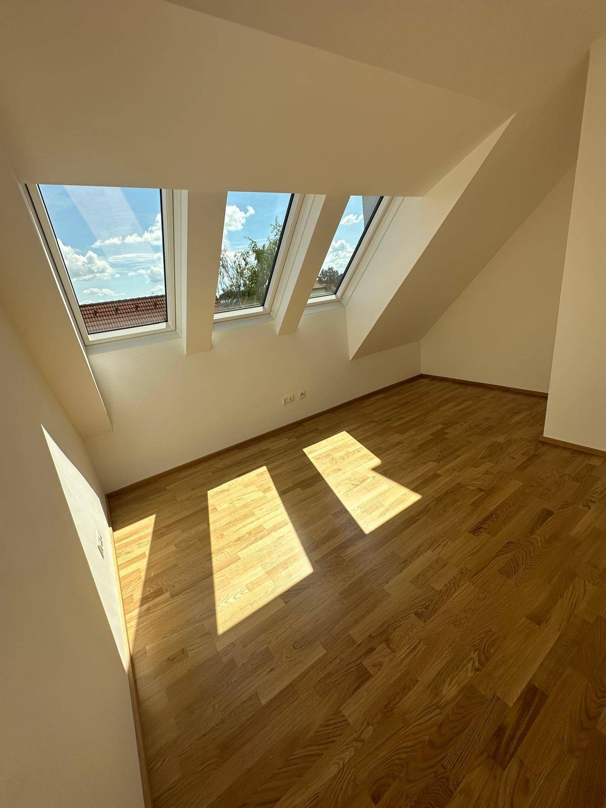 Lichtdurchflutetes Schlafzimmer mit Parkettboden und mehreren Dachfenstern.