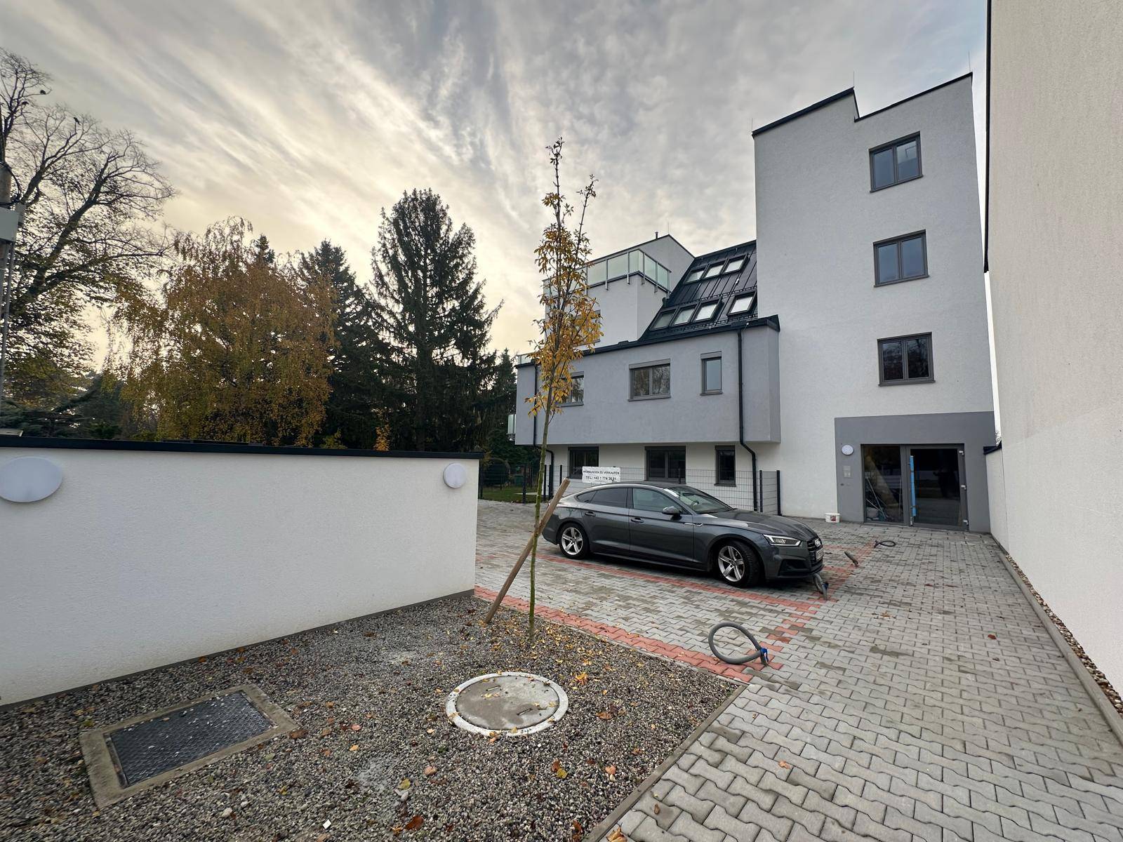 Seitenansicht des Neubaus mit Parkplatz und Zufahrt auf gepflastertem Gelände.