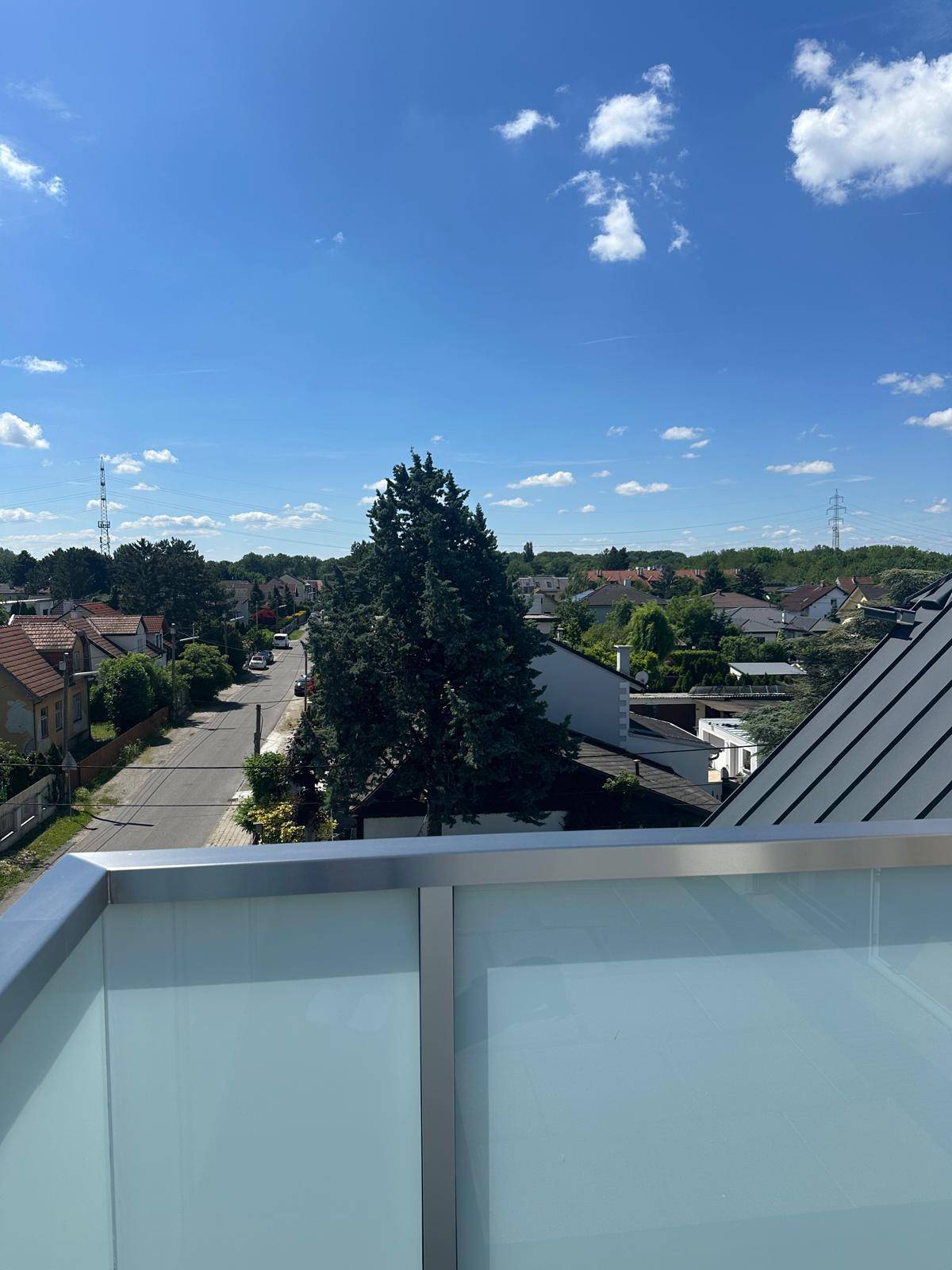 Sonniger Balkon mit Glasgeländer und Blick auf die umliegende Wohngegend.