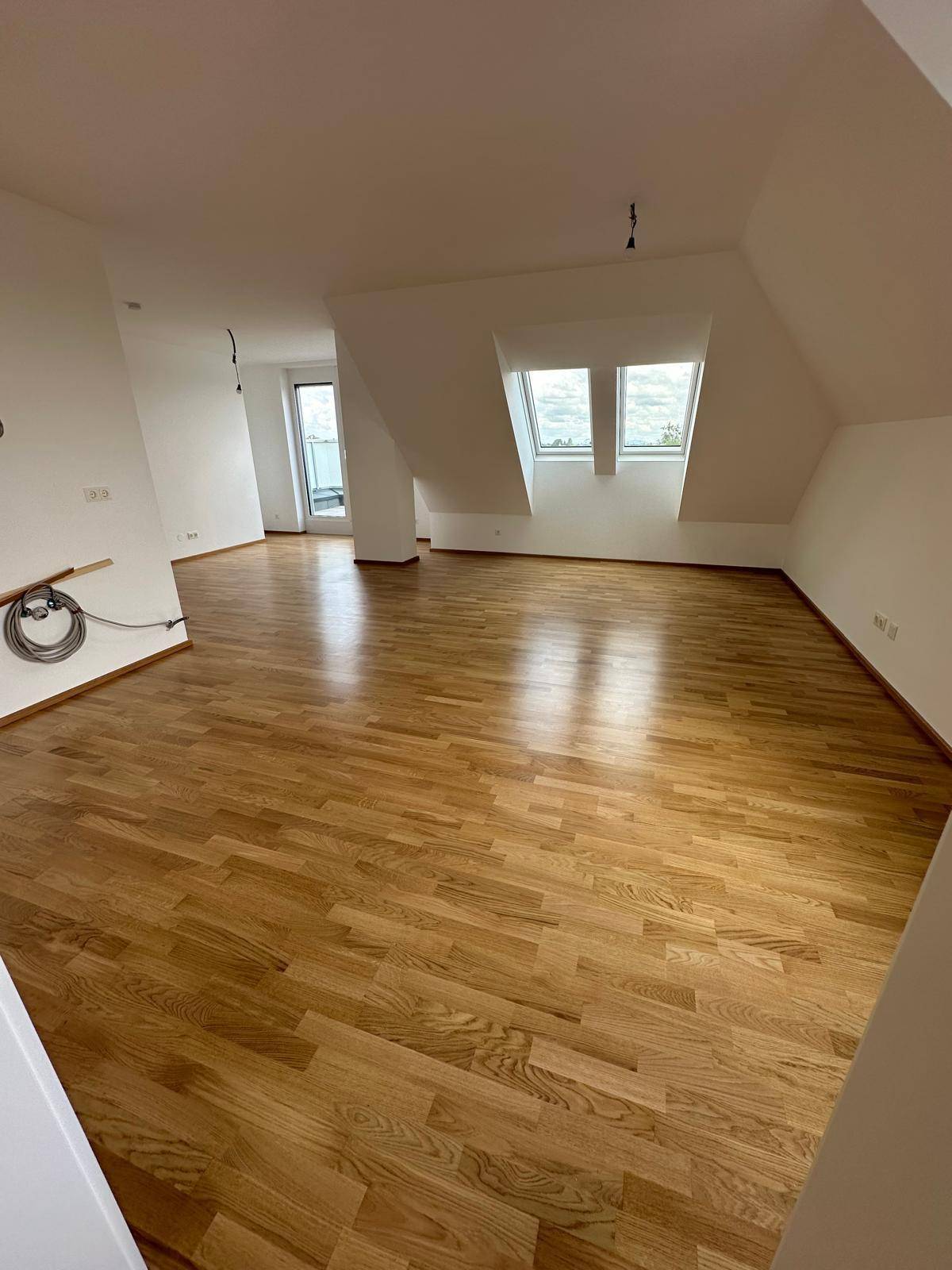 Großes, helles Wohnzimmer mit Holzboden, Dachfenstern und Zugang zu einer Außenterrasse.