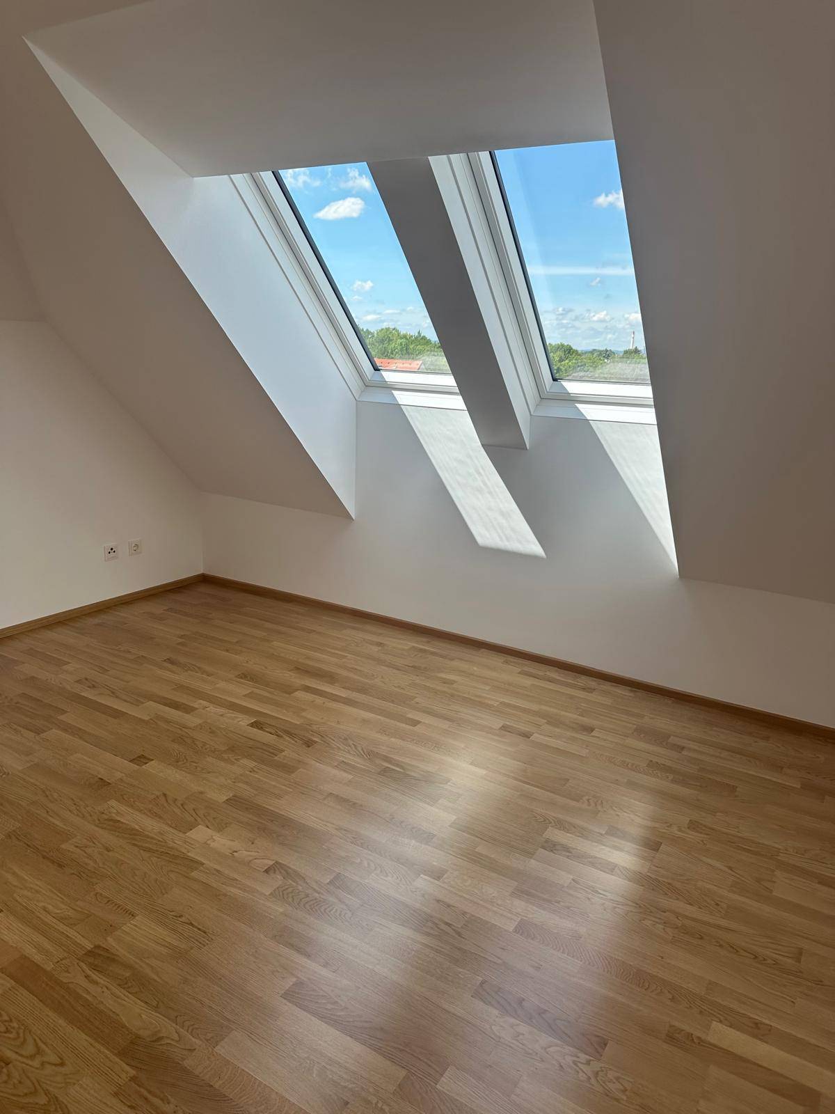Helles Schlafzimmer mit Parkettboden und großen Dachfenstern unter der Schräge.