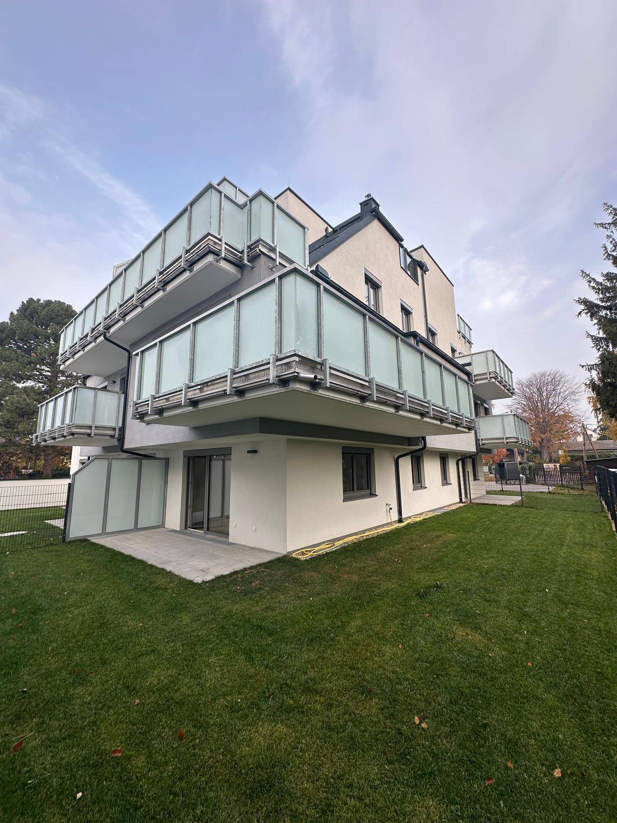 Neubau mit Balkonen, Terrasse und gepflegter Rasenfläche im Gartenbereich.