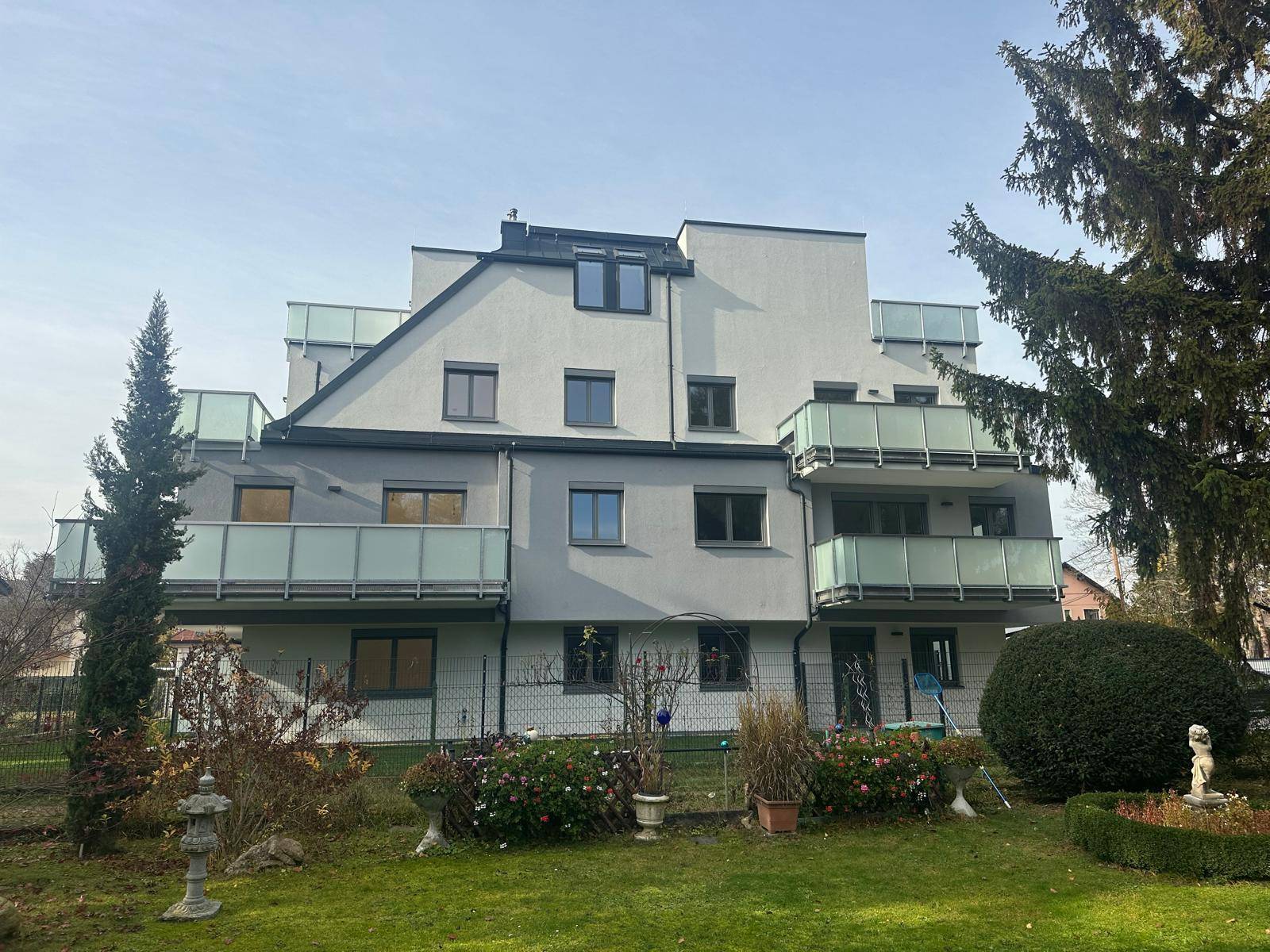 Rückansicht des modernen Wohnhauses mit mehreren Balkonen und einem gepflegten Gartenbereich.
