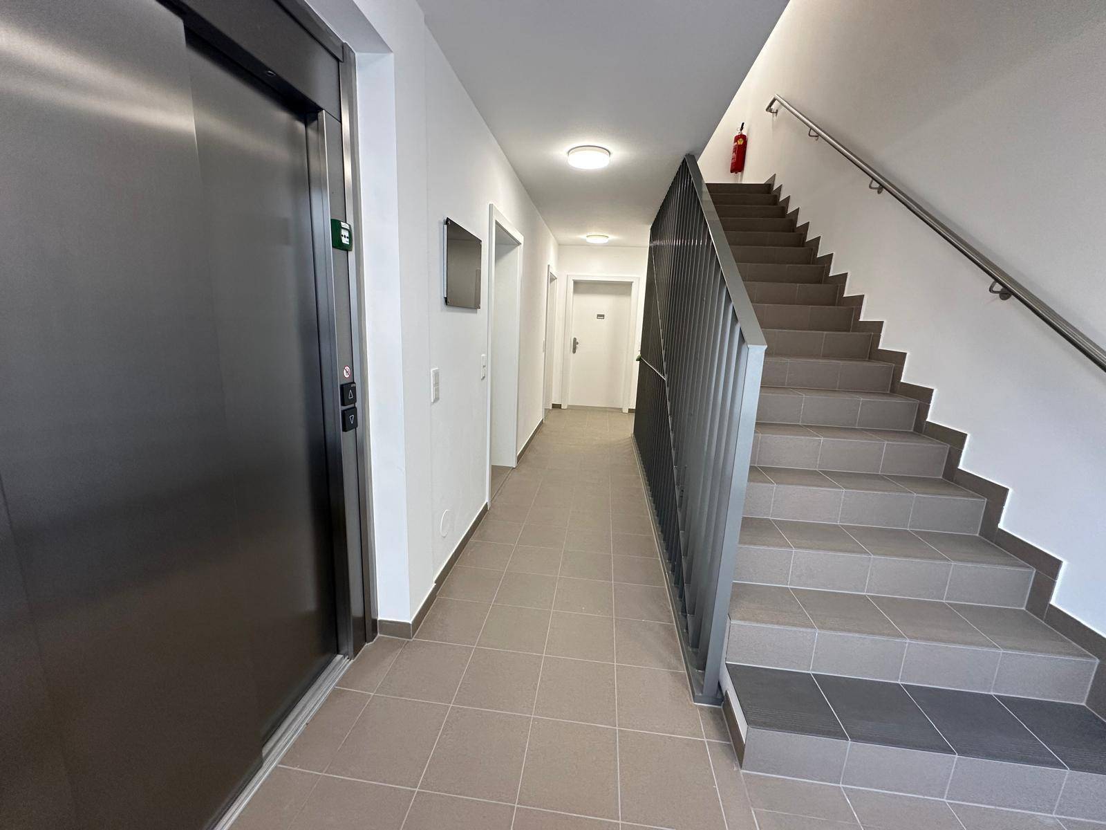 Treppenhaus und Aufzug in einem Mehrfamilienhaus mit Fliesenboden.