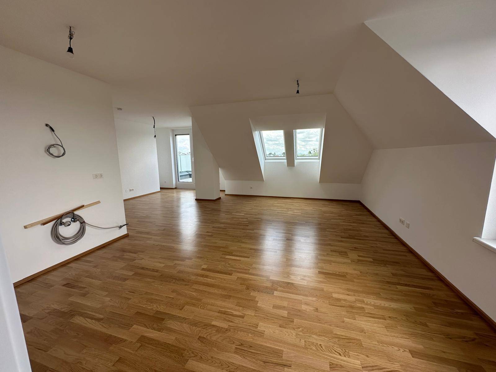 Geräumiges Wohnzimmer im Dachgeschoss mit Holzboden, Dachschrägen und Zugang zu einem Balkon.
