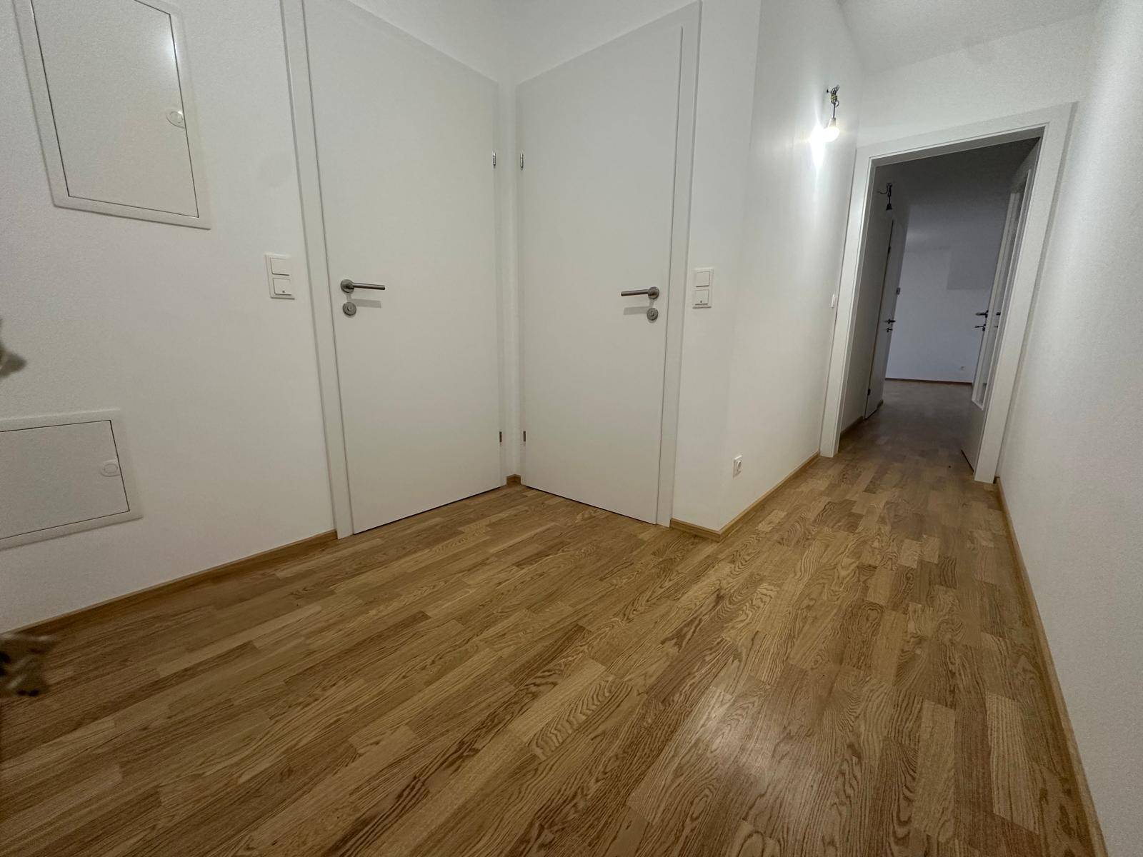 Heller Flur mit hellem Holzfußboden und weißen Türen, der zu weiteren Räumen führt.