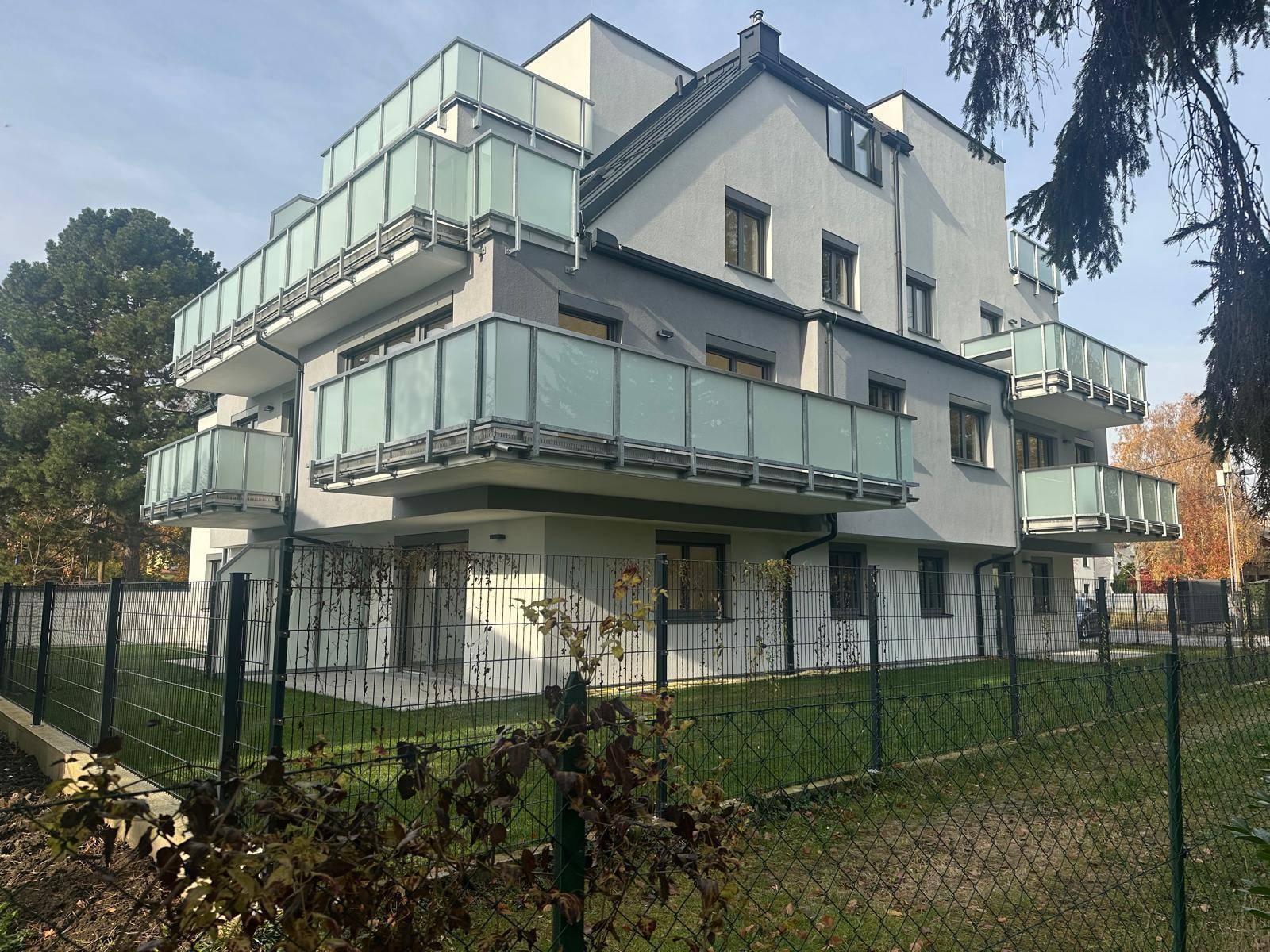 Seitenansicht des Neubaus mit zahlreichen Balkonen und einem umzäunten Gartenbereich.