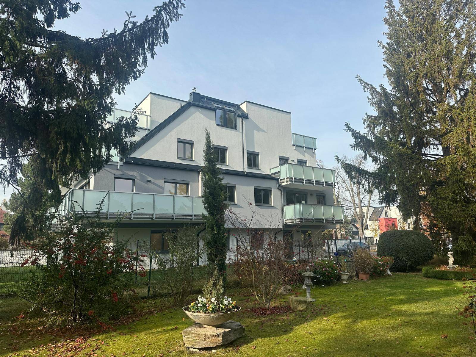 Weitläufiger Gartenbereich hinter dem modernen Gebäude mit verschiedenen Pflanzen und Balkonen.