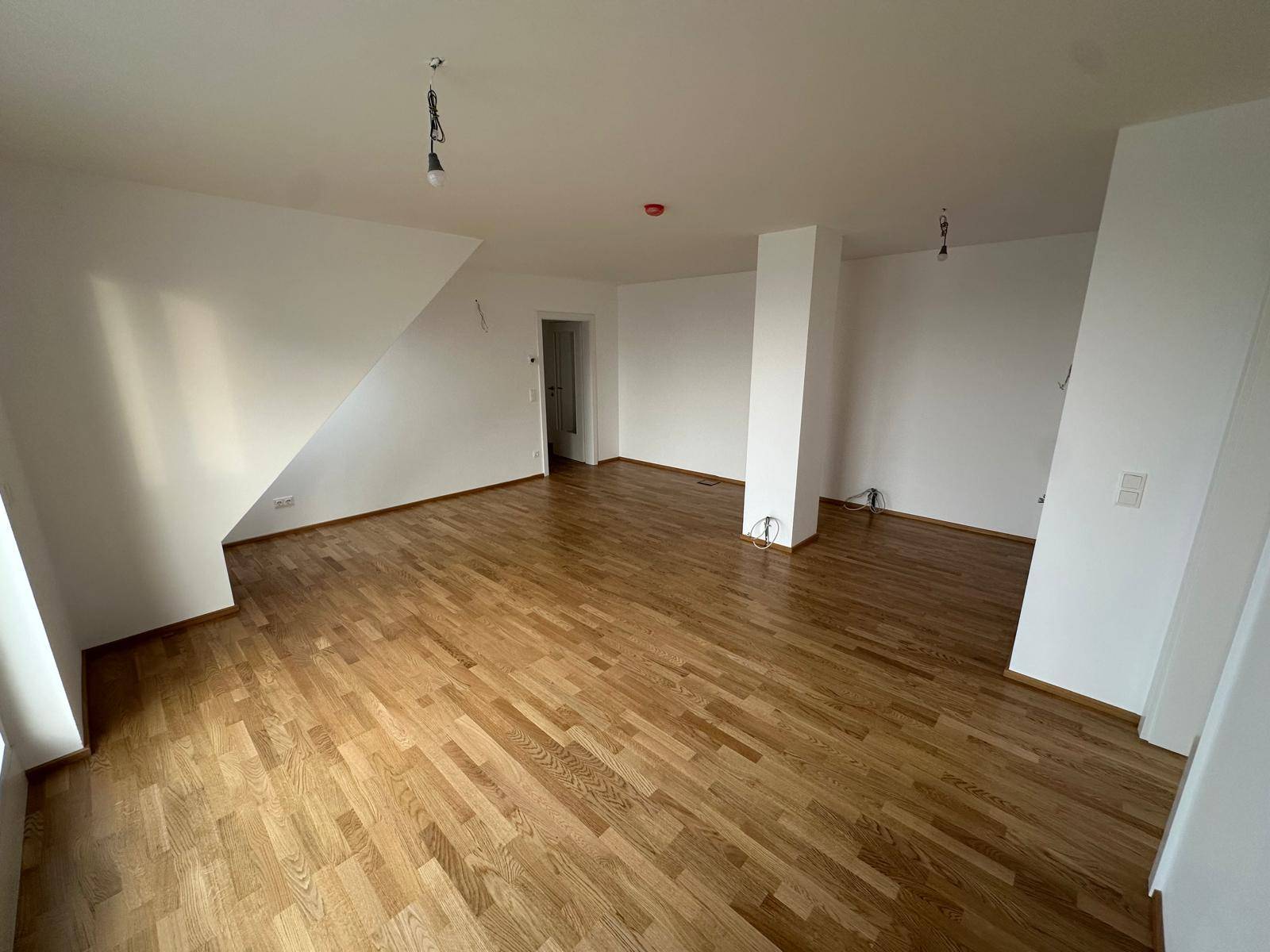 Geräumiger, heller Wohnbereich mit Holzboden und mehreren Zugängen zu anderen Räumen.
