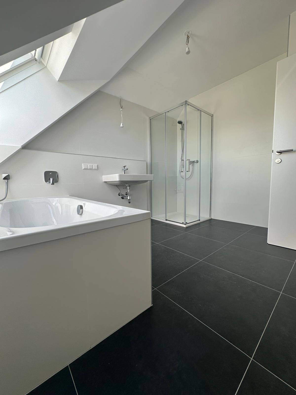 Geräumiges Badezimmer mit Badewanne, Duschkabine und dunklem Fliesenboden.