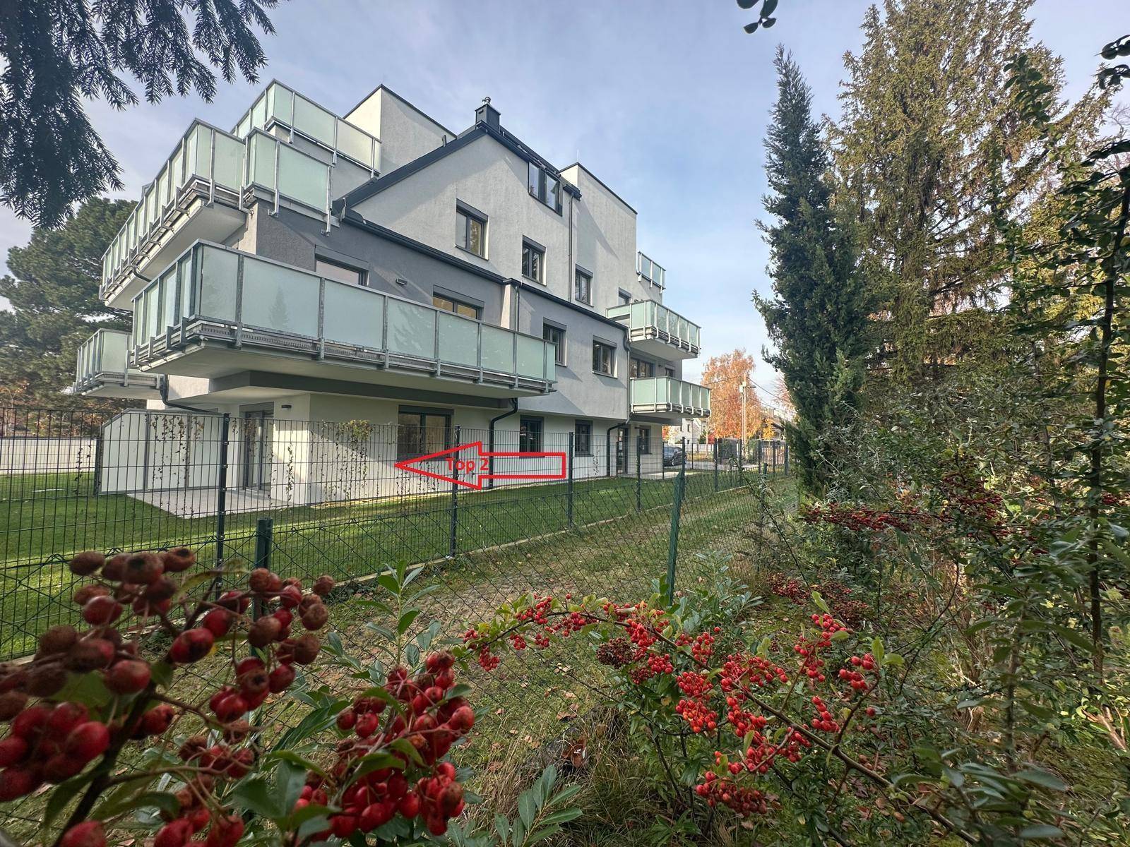 Modernes Wohngebäude mit Balkonen und einem grünen Garten, ein Pfeil weist auf einen Bereich.