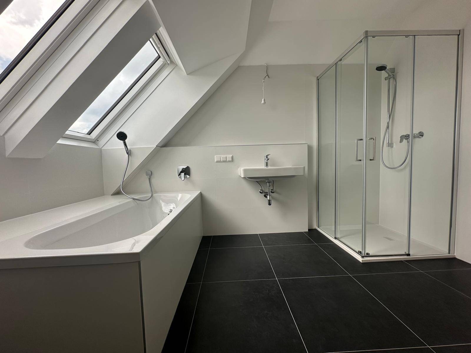 Modernes Badezimmer im Dachgeschoss mit Badewanne, Dusche, Waschbecken und großem Dachfenster.
