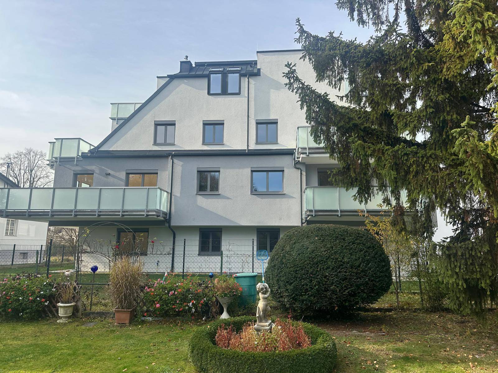 Rückansicht des Wohnhauses mit Garten, Hecken und Balkonen unter hellem Himmel.