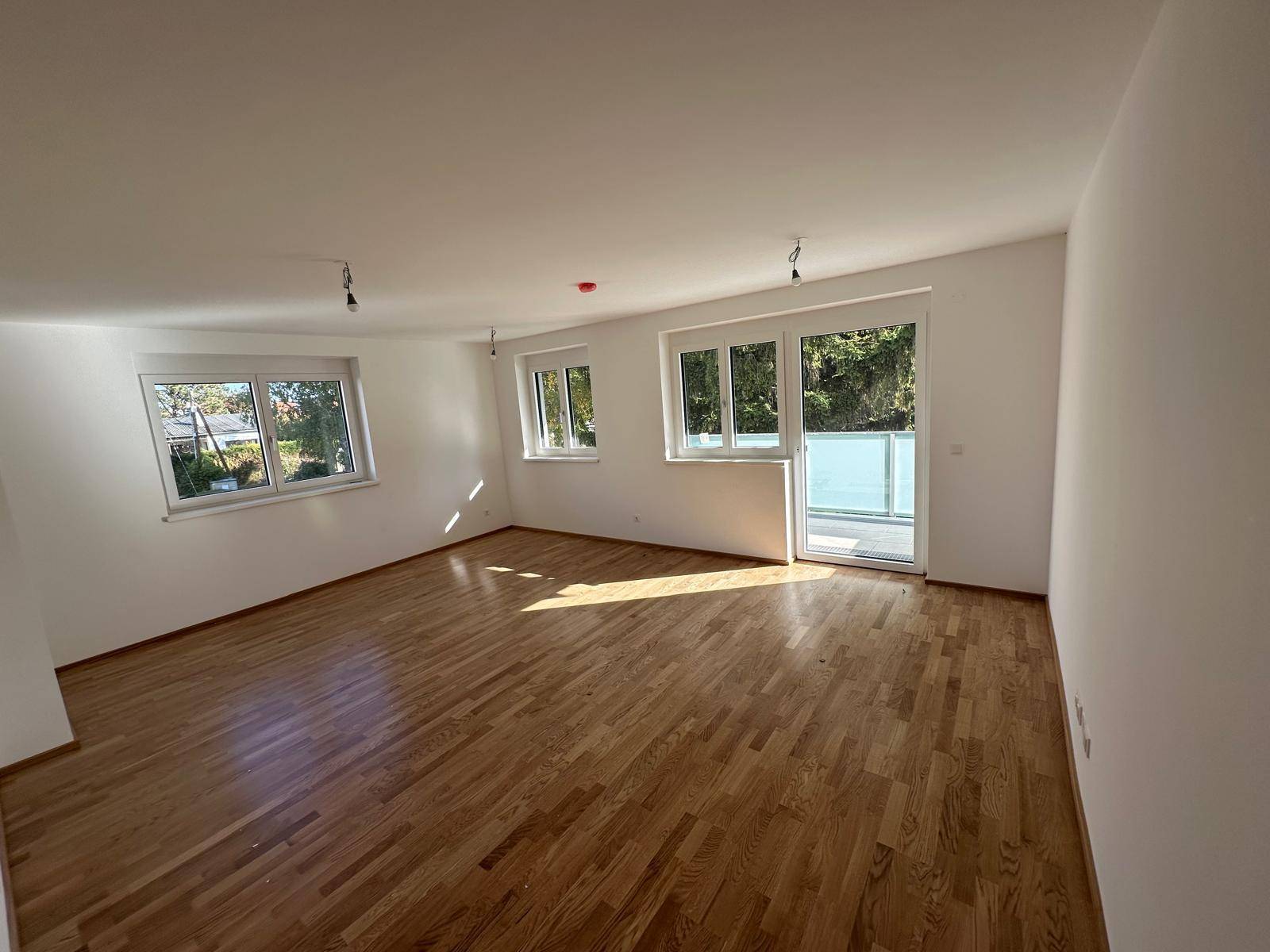 Geräumiger Wohnbereich mit hellem Parkettboden und großen Fenstern für viel Tageslicht.