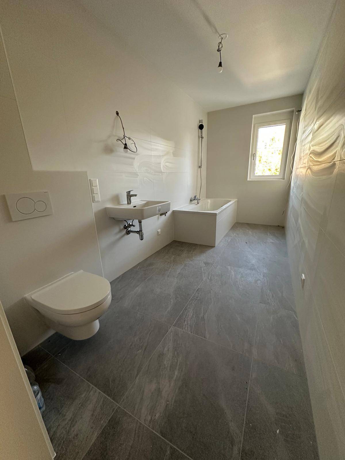 Modernes Badezimmer in Neubauqualität mit Badewanne, WC und großformatigen Fliesen.