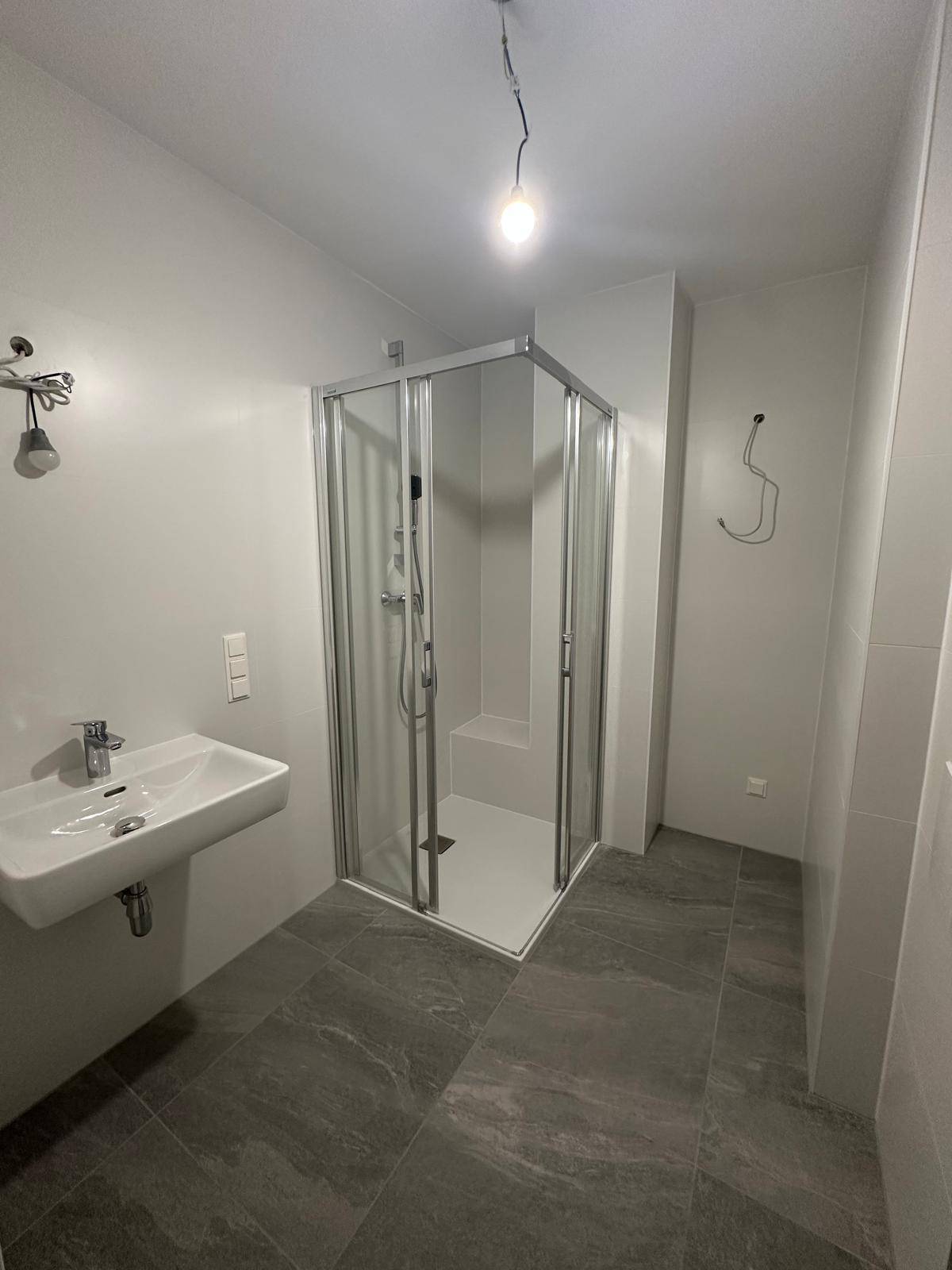 Modernes Badezimmer mit Duschkabine, Waschbecken und grauen großformatigen Fliesen.