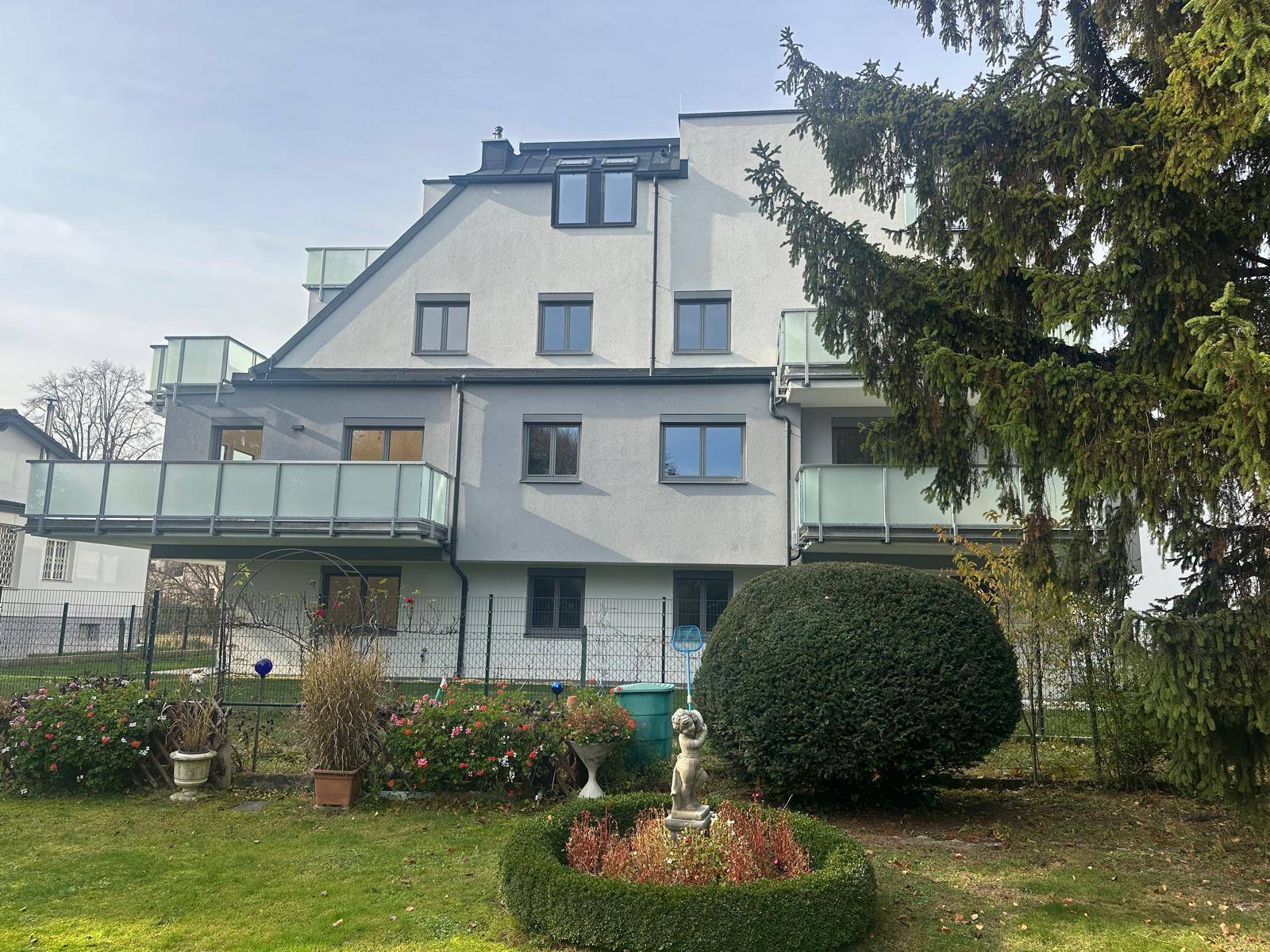 Gepflegter Gartenbereich hinter dem modernen Gebäude mit Blumenbeeten und Balkonen.