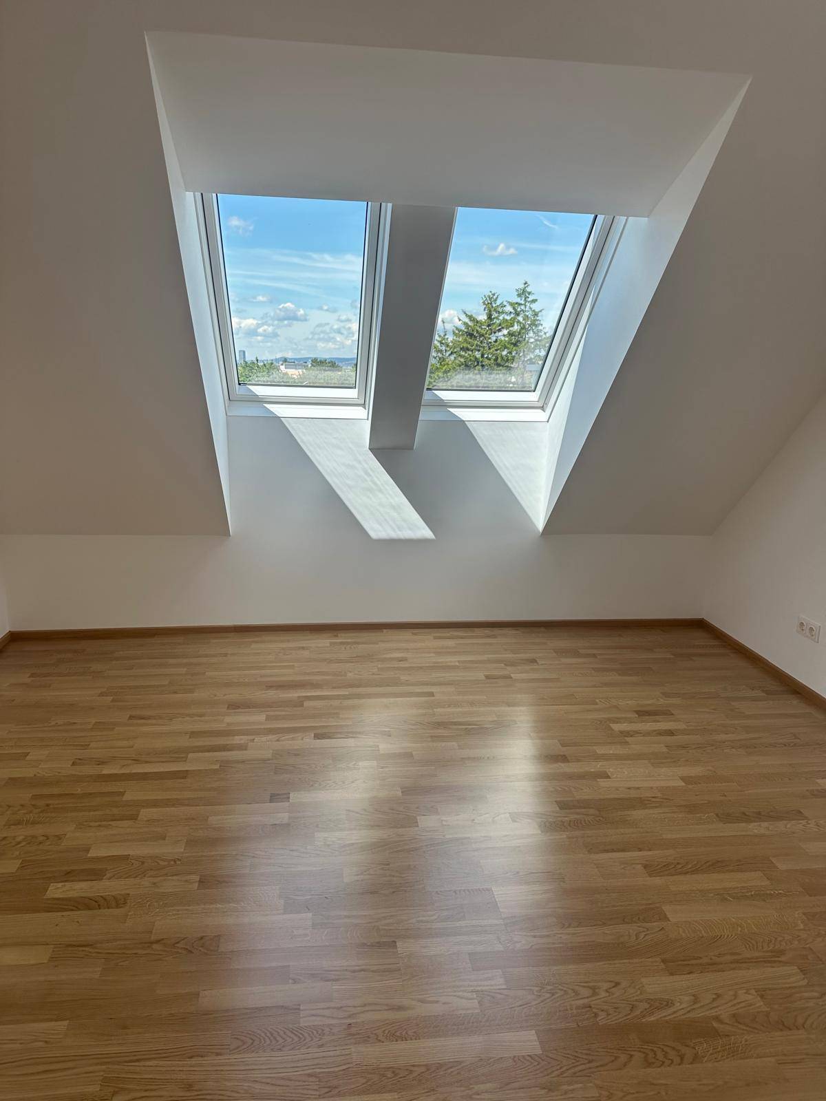 Geräumiges Dachzimmer mit Holzboden und zwei Dachfenstern, die einen Blick ins Grüne bieten.