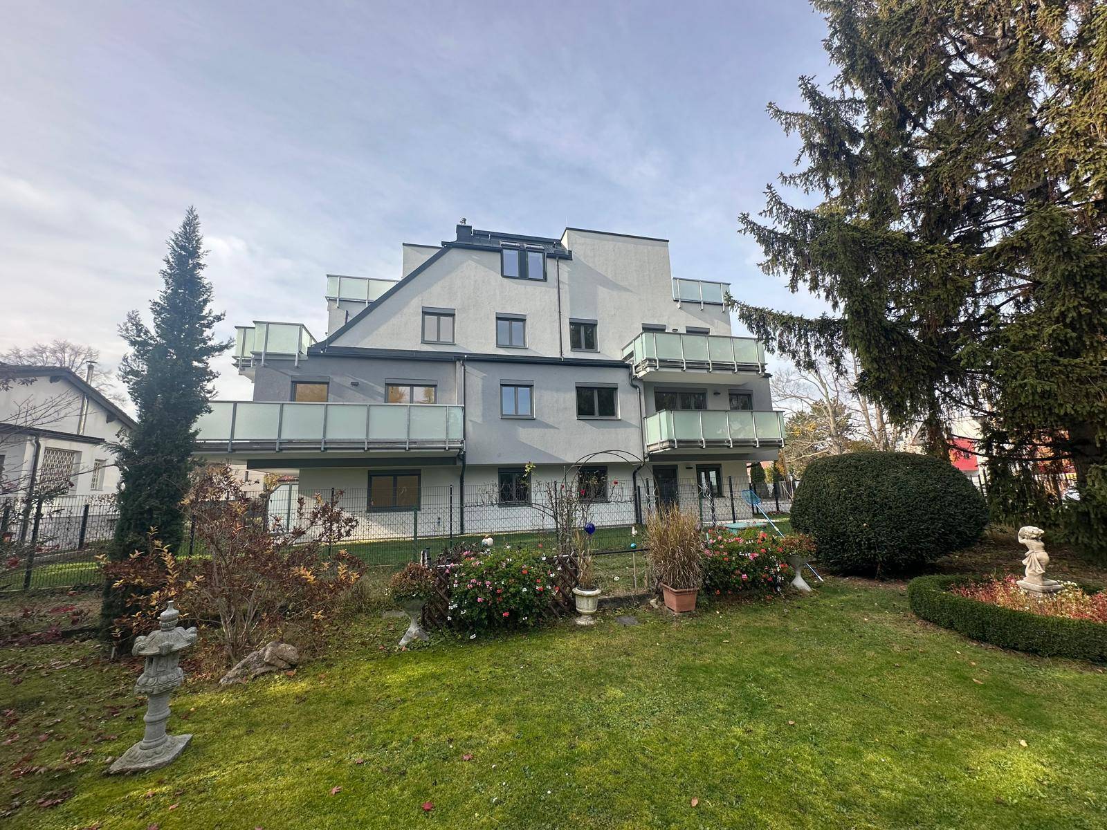 Gepflegter Gartenbereich vor dem modernen Wohngebäude mit Balkonen und Bäumen.