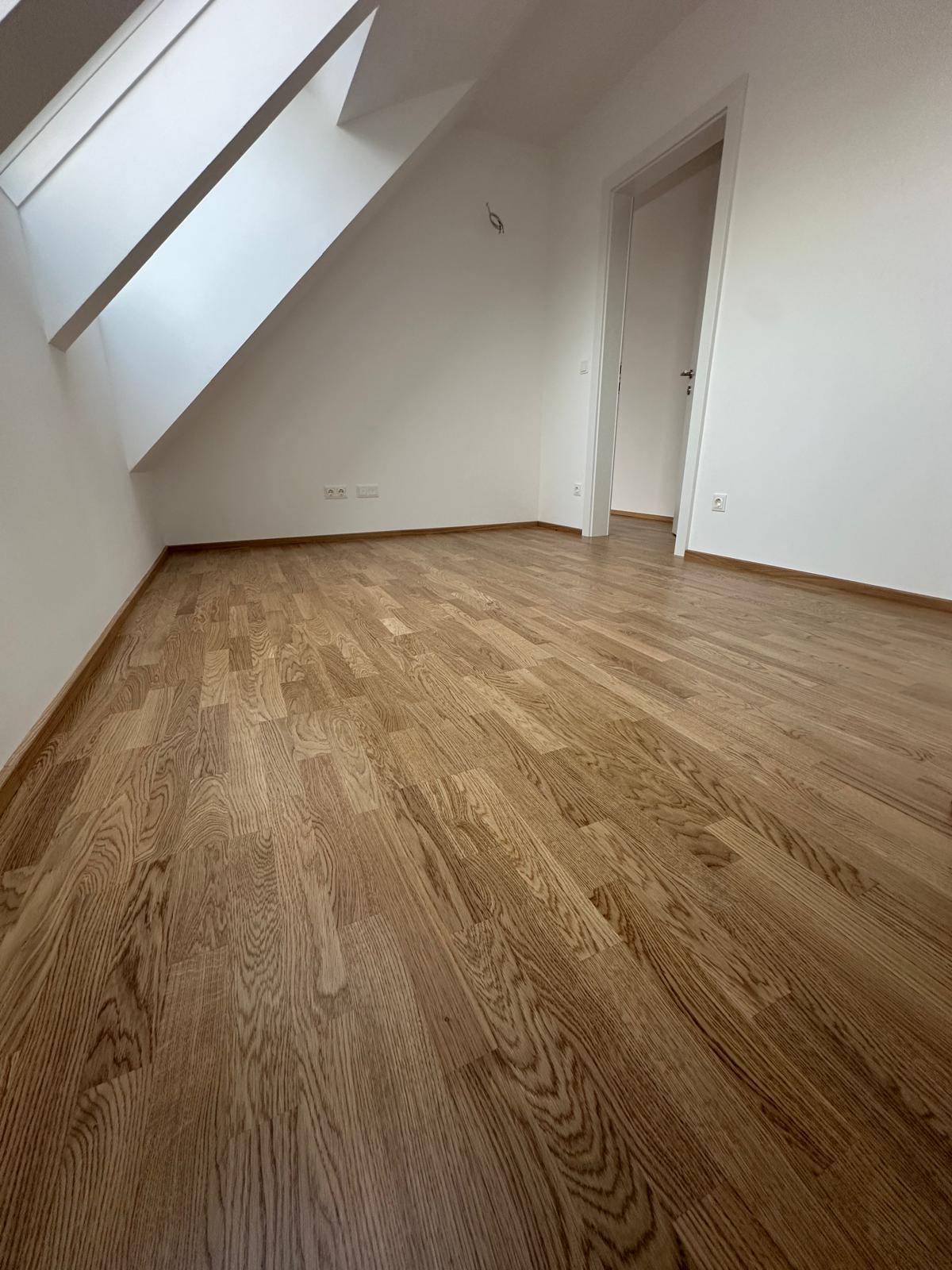 Helles Dachzimmer mit Holzboden, weißen Wänden und Dachfenstern für viel Tageslicht.