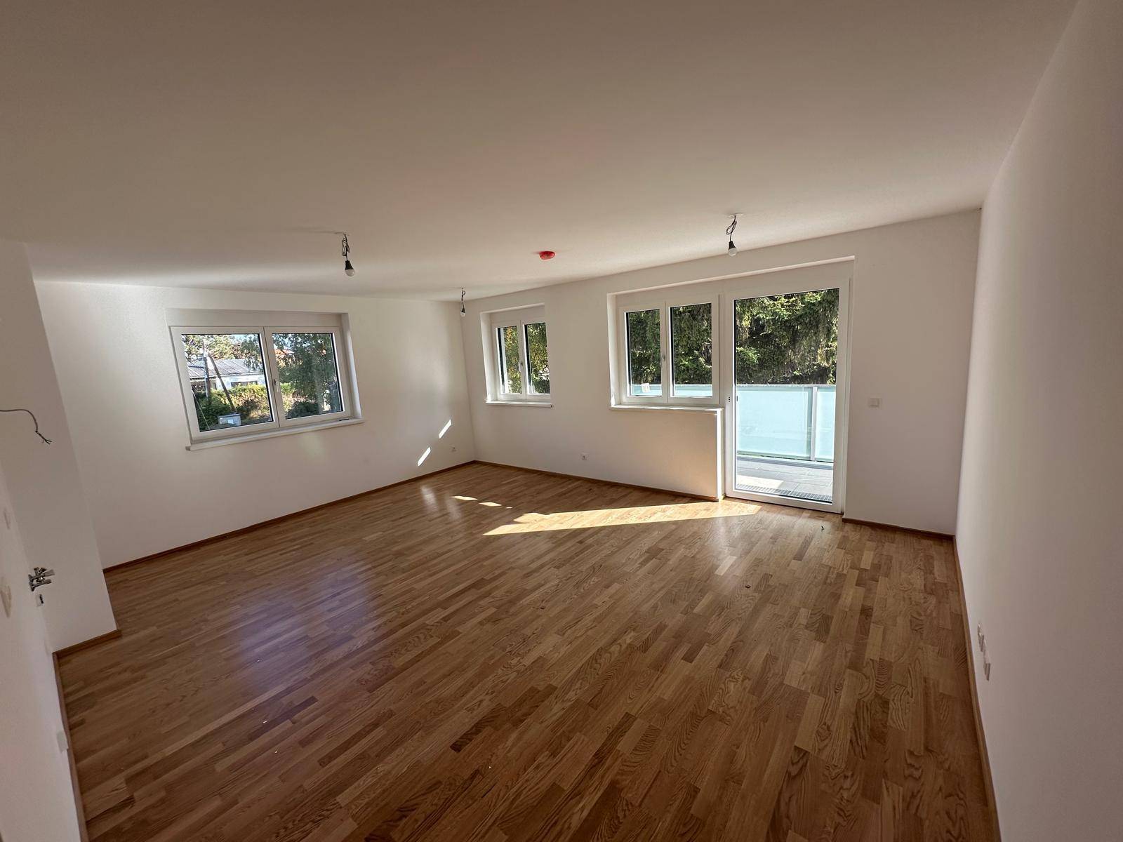 Lichtdurchfluteter Wohnbereich mit Parkettboden und Zugang zu einem Balkon.