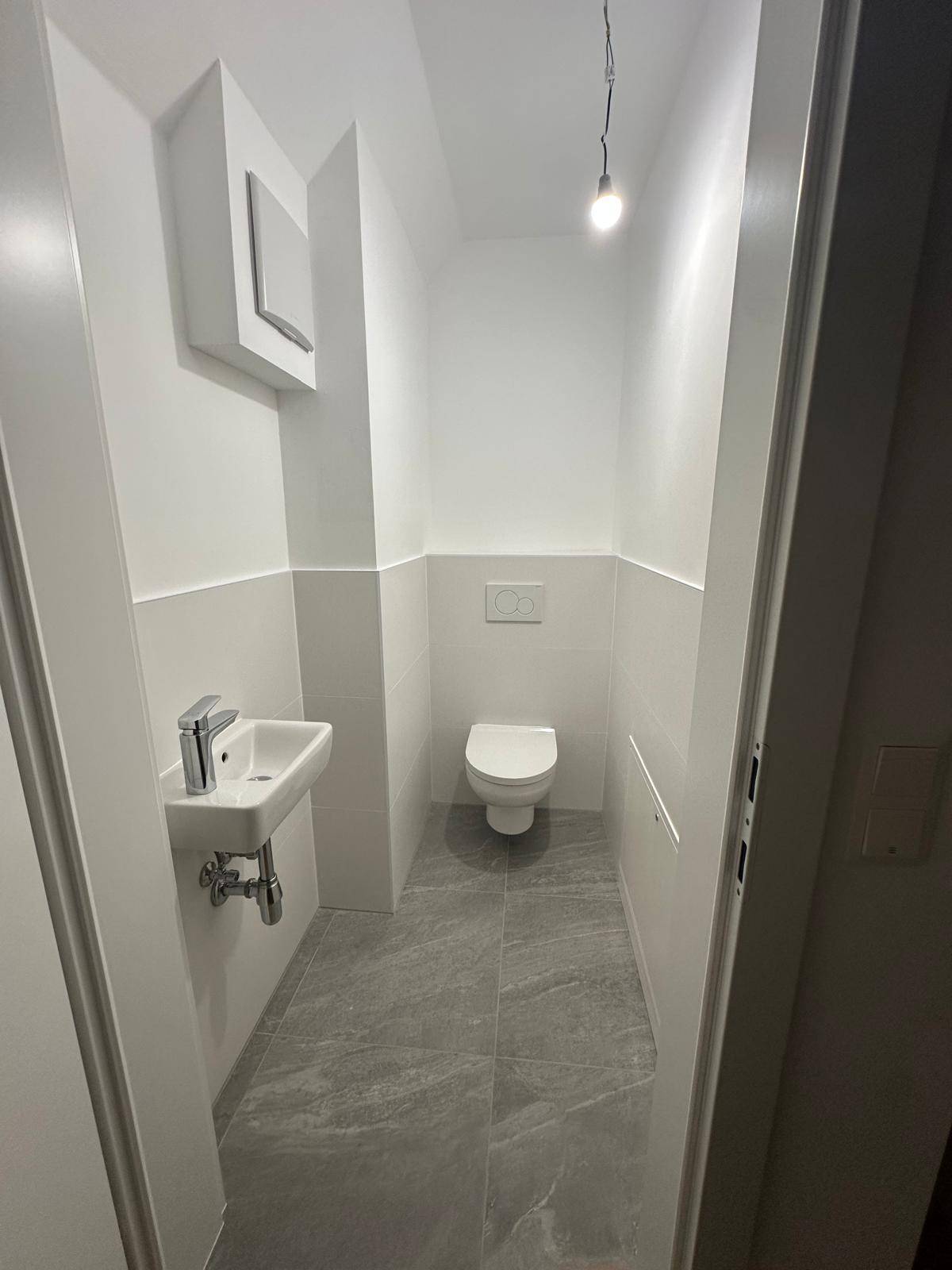 Kleines Gäste-WC mit modernen grauen Fliesen, wandhängendem WC und Handwaschbecken.