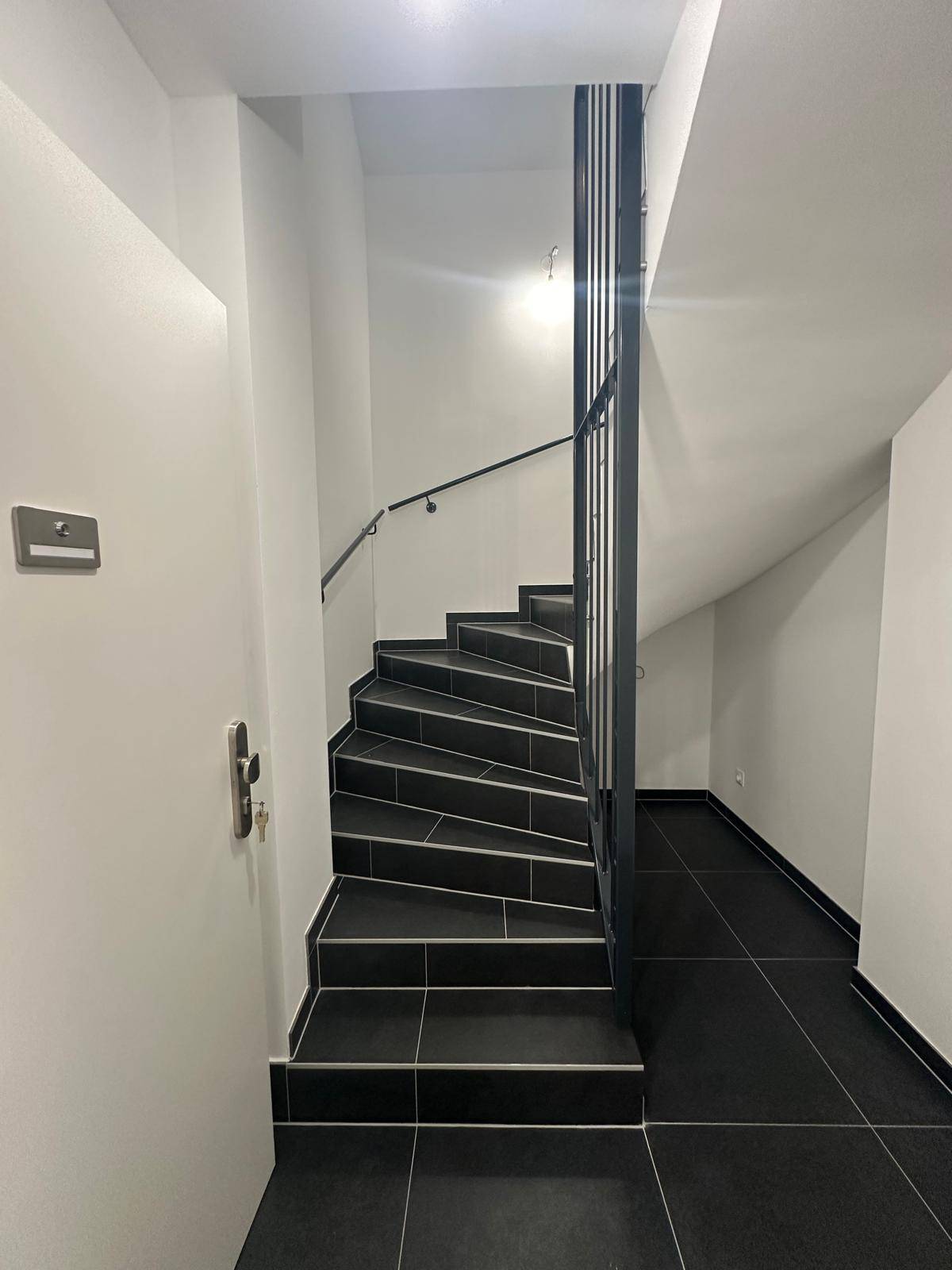 Modernes Treppenhaus mit dunklen Fliesen und elegantem Geländer.