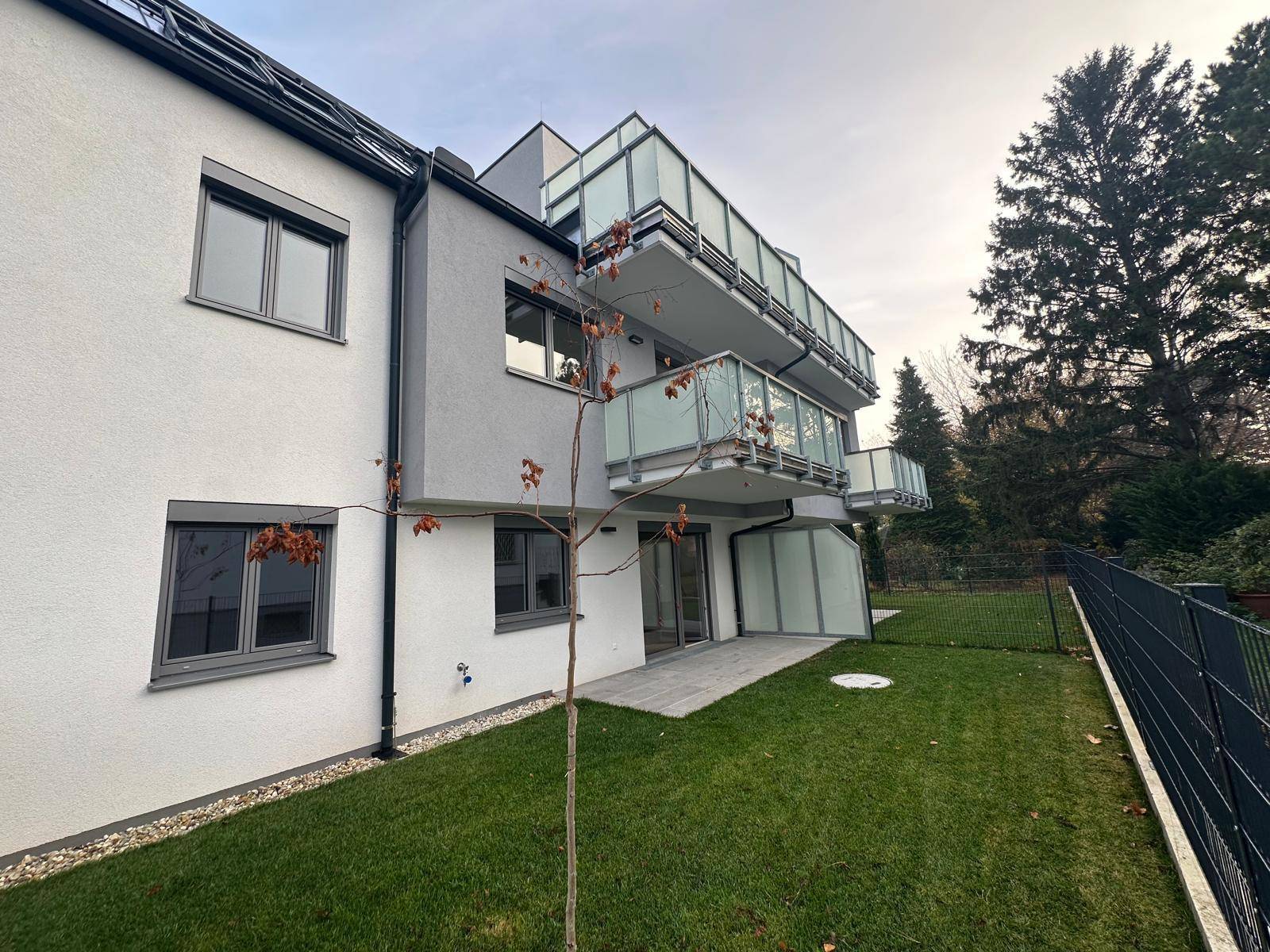Modernes Mehrfamilienhaus mit Balkonen, Glasbrüstungen und einer kleinen Rasenfläche im Außenbereich.