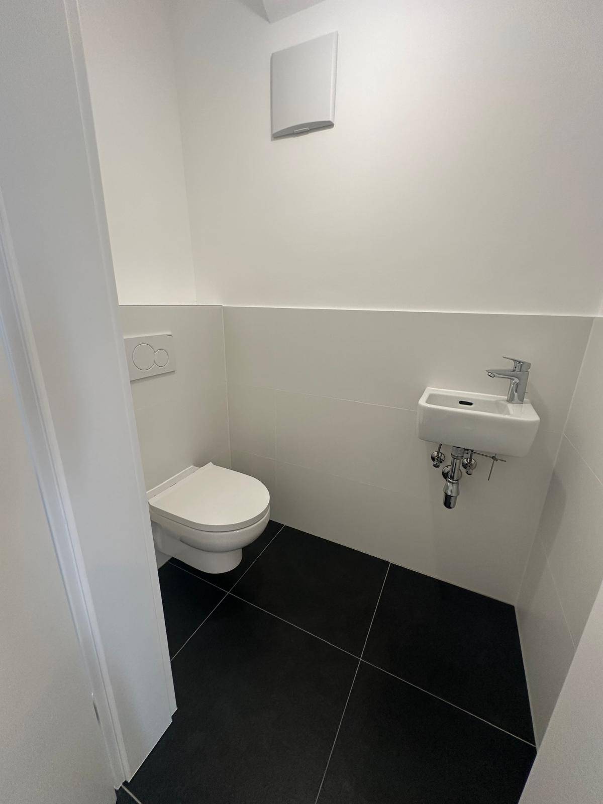 Modernes Gäste-WC mit weißen Wandfliesen, schwarzem Boden und wandhängendem WC.