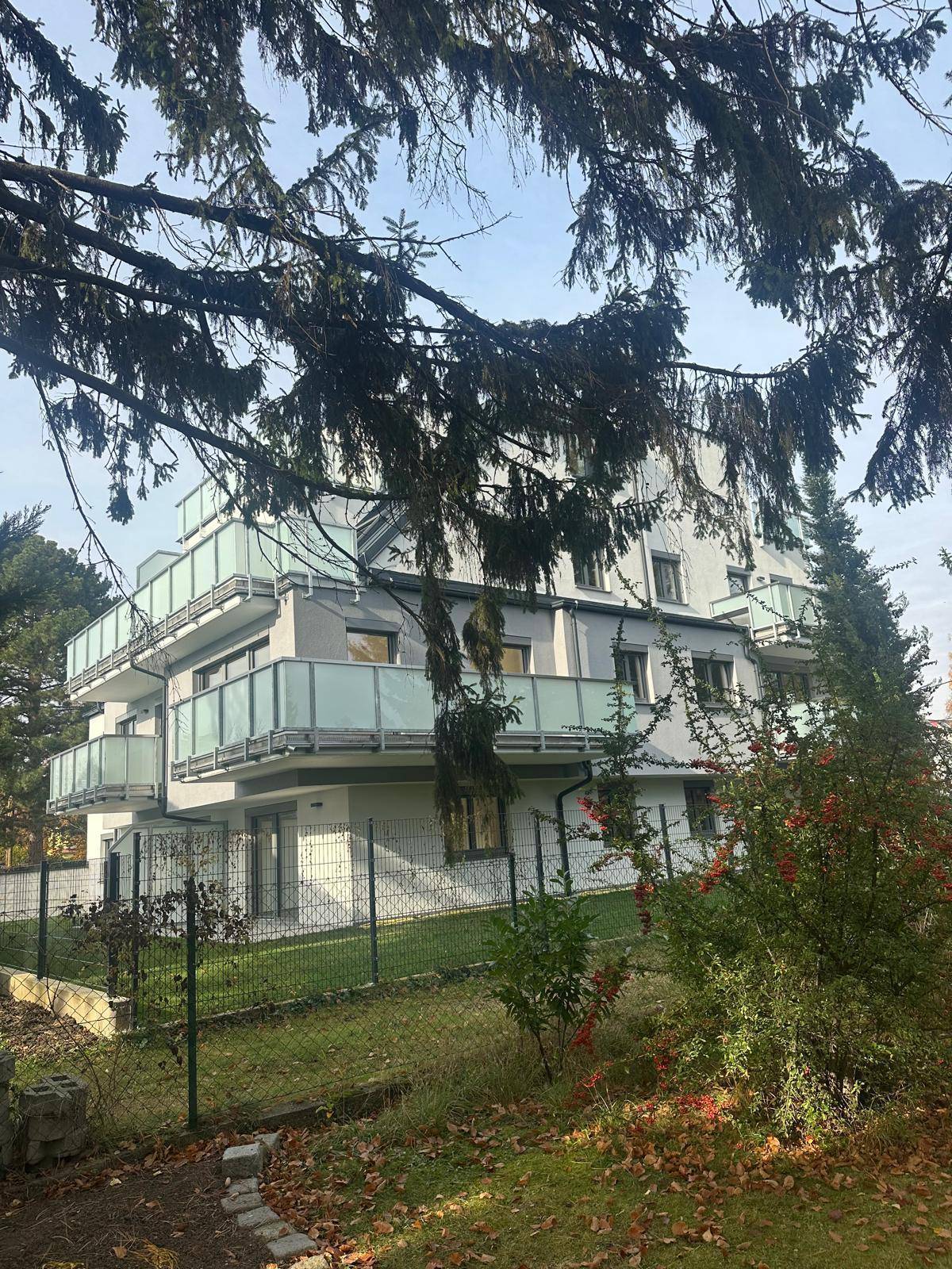 Modernes Wohngebäude mit Balkonen, umgeben von einem grünen, gepflegten Garten.