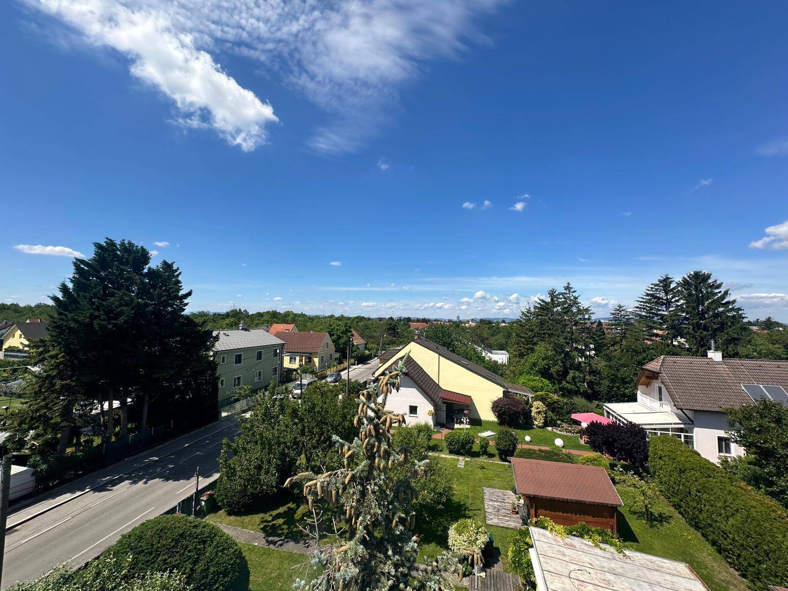 Weitläufiger Blick über eine grüne Wohngegend mit Häusern und viel Natur unter blauem Himmel.