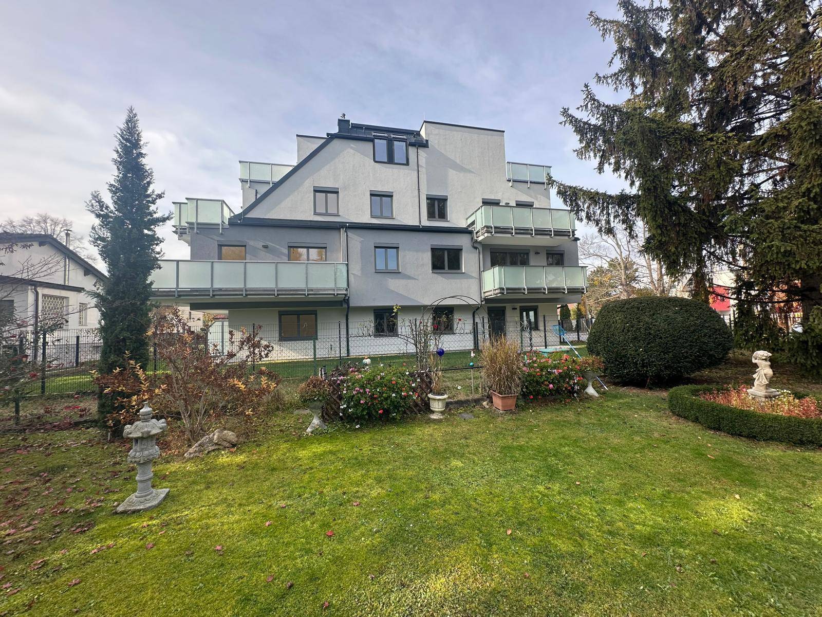 Rückansicht des modernen Wohnhauses mit Balkonen und einem weitläufigen, grünen Garten.