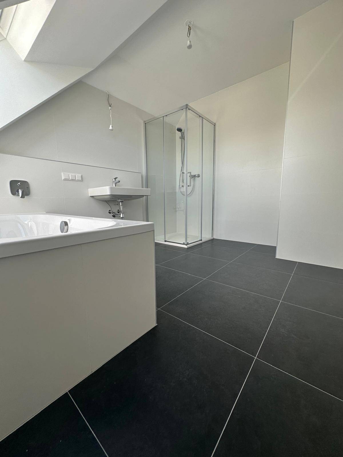 Modernes Badezimmer mit dunklen Fliesen, Badewanne und Duschkabine unter Dachschräge.
